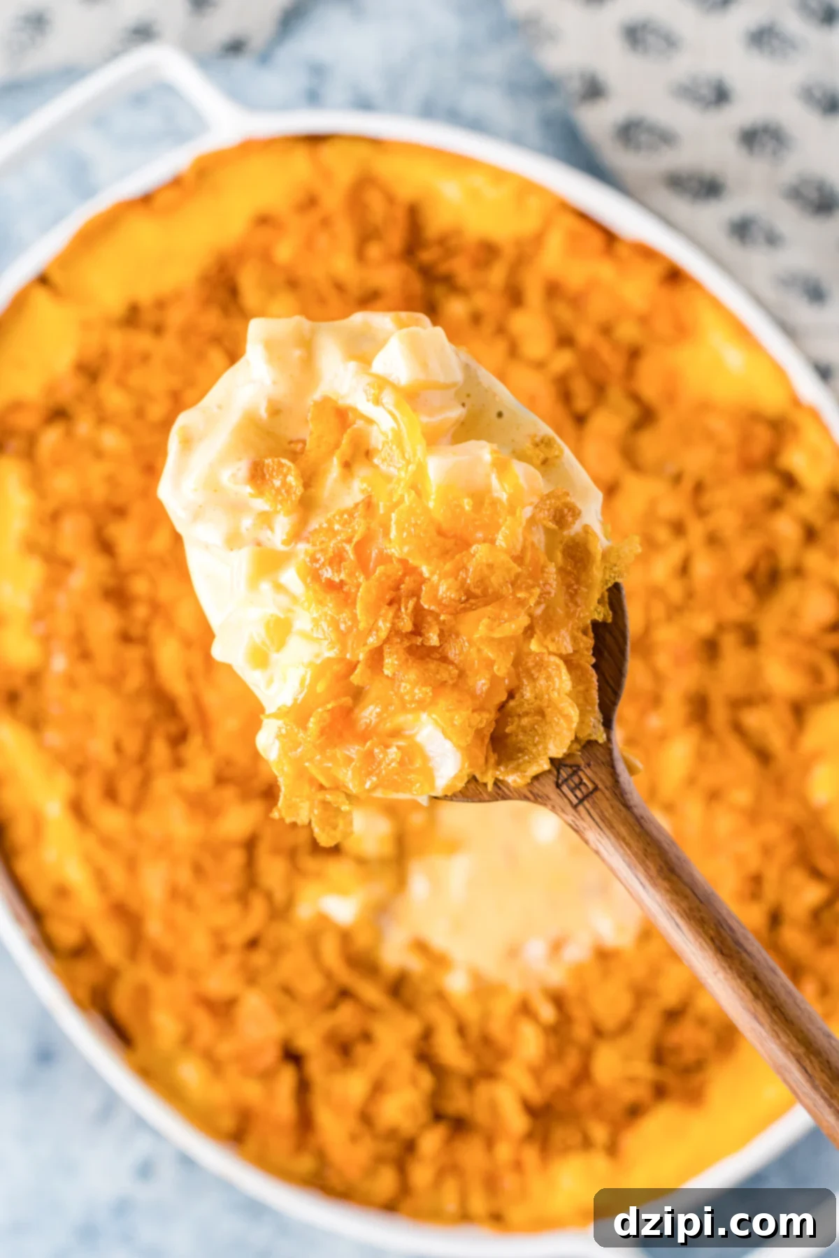 A wooden spoon is filled with funeral potatoes. The casserole dish is out of focus in the background.