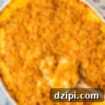 Overhead view of white oval baking dish filled with orange, cheesy funeral potatoes topped with cornflakes.
