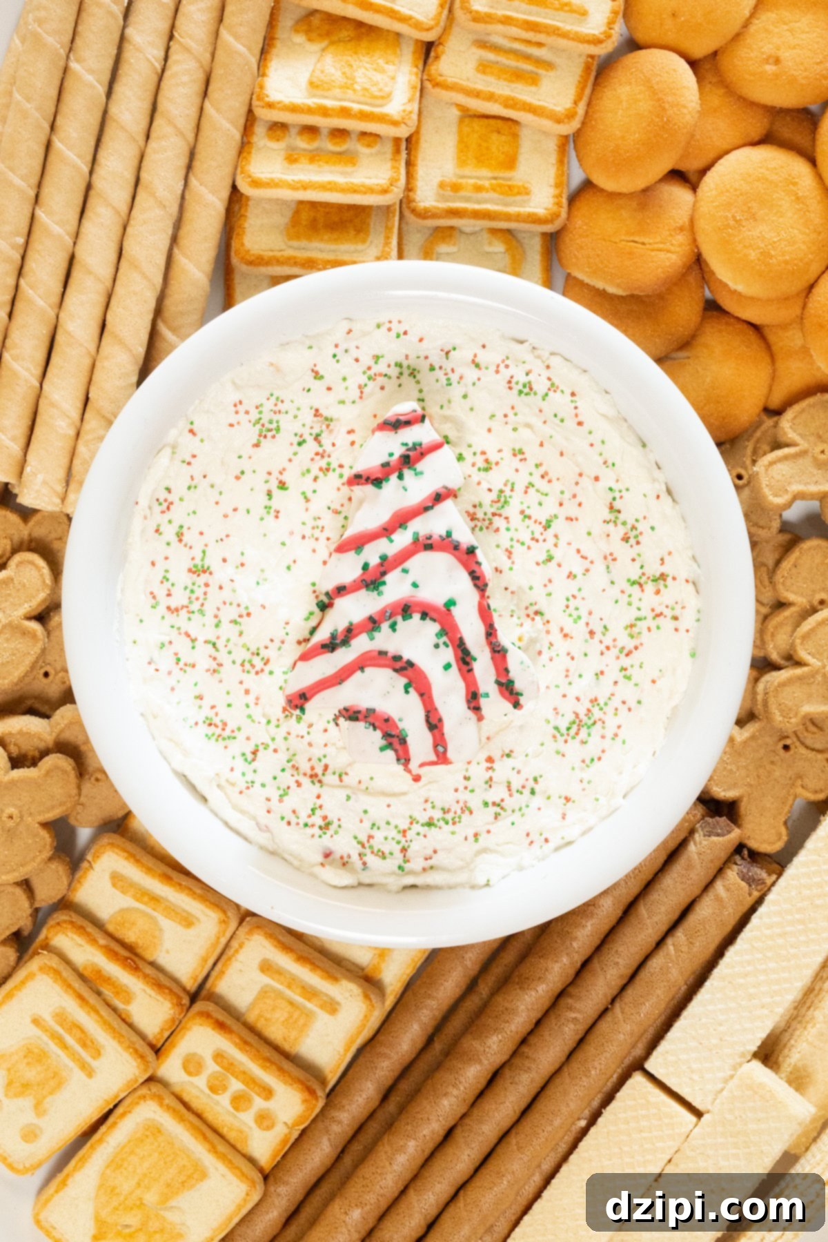 Holiday Tree Cake Dip 3 An overhead shot showcasing a beautiful holiday platter centered with a bowl of homemade Little Debbie's Christmas Tree Cake Dip, surrounded by an inviting array of various cookies ready for dipping.