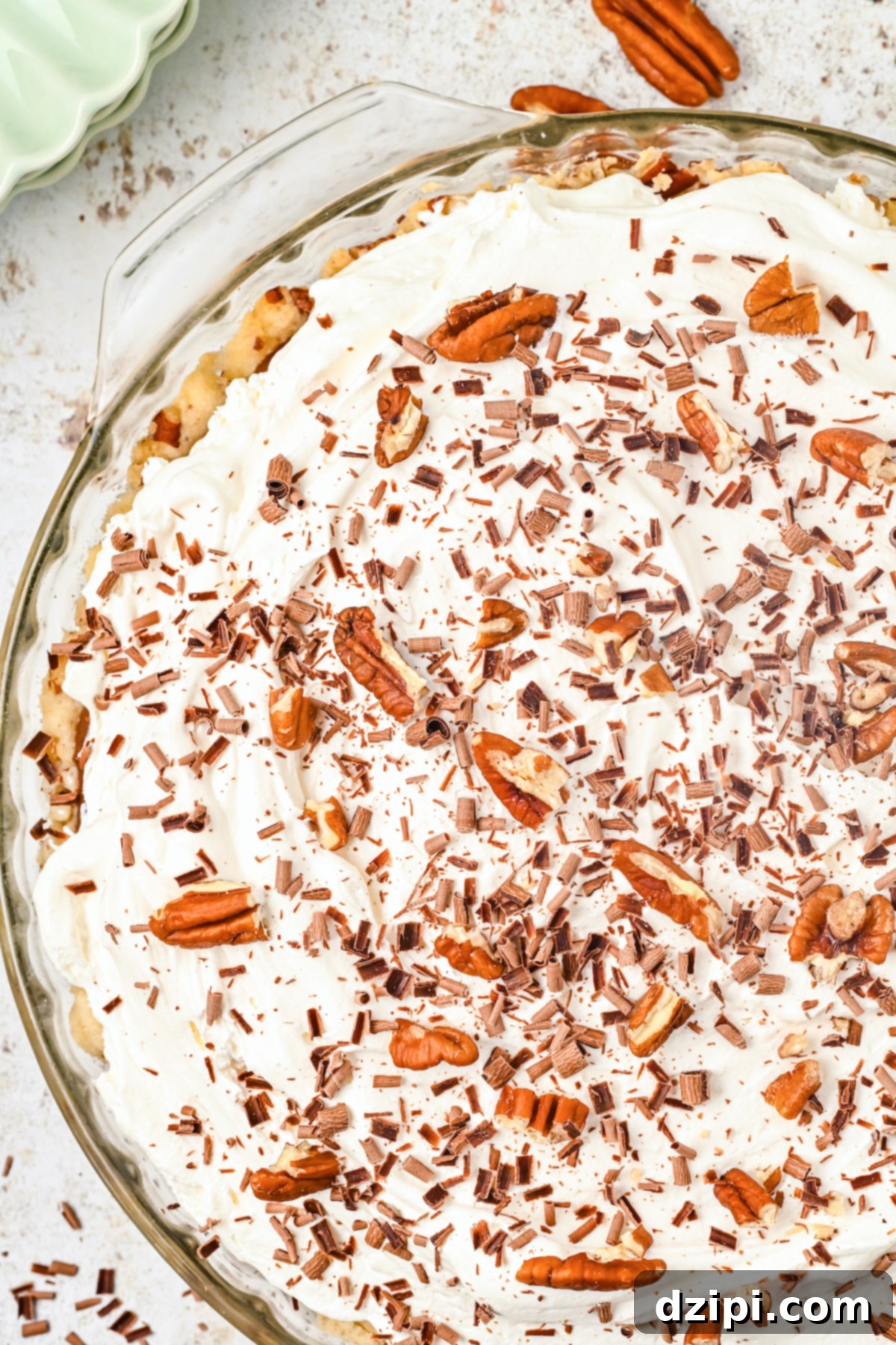 A glass pie dish filled with a possom pie that's topped with cool whip and roughly chopped pecans.