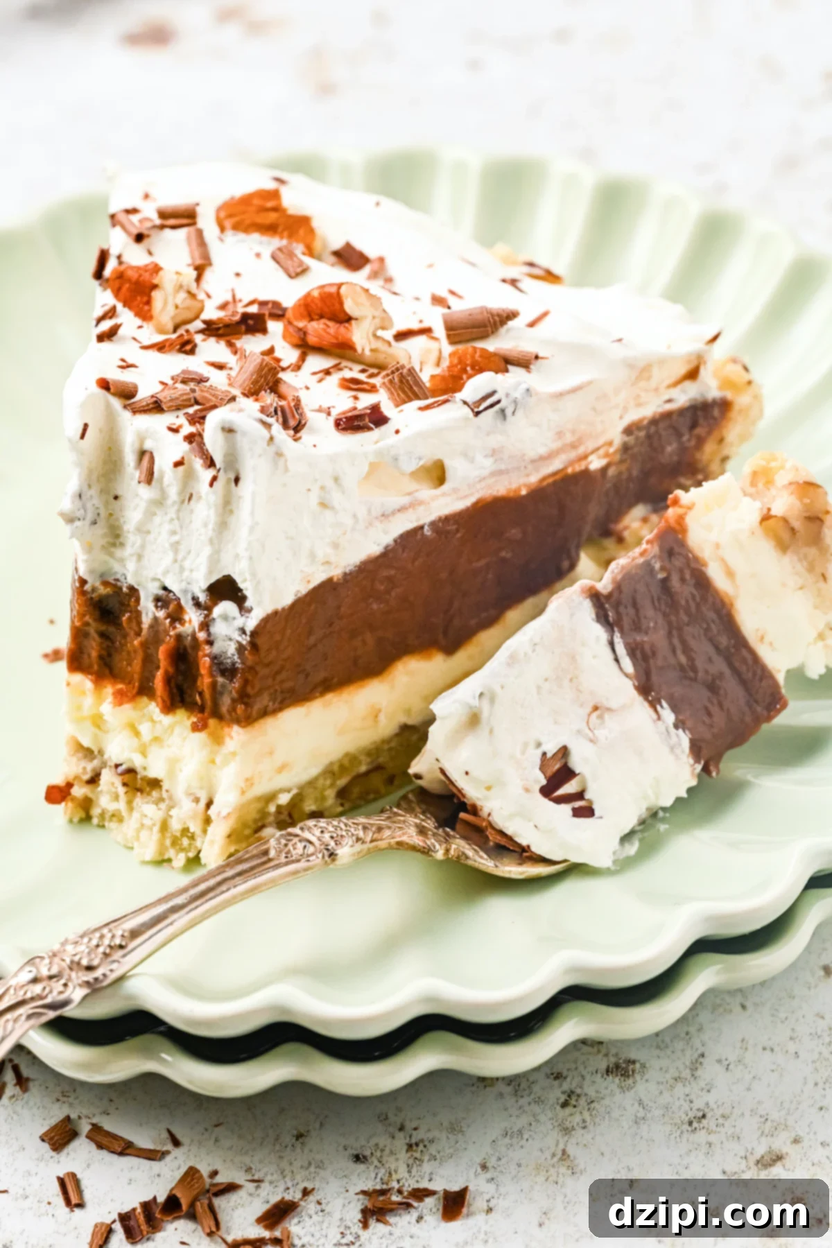 A slice of layered possum pie sits on a pale green serving dish. A fork with the end of the pie on it rests next to the slice.