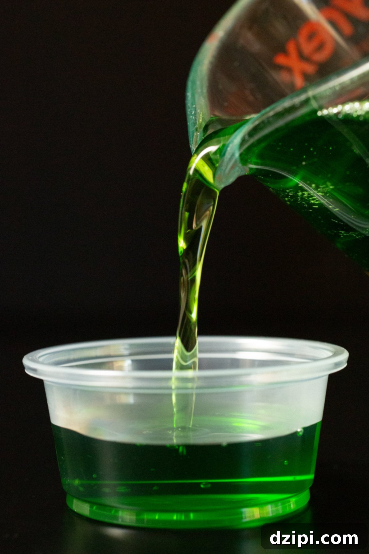 Liquid green apple gelatin and Crown mixture being poured into a 2 oz jello shot cup.