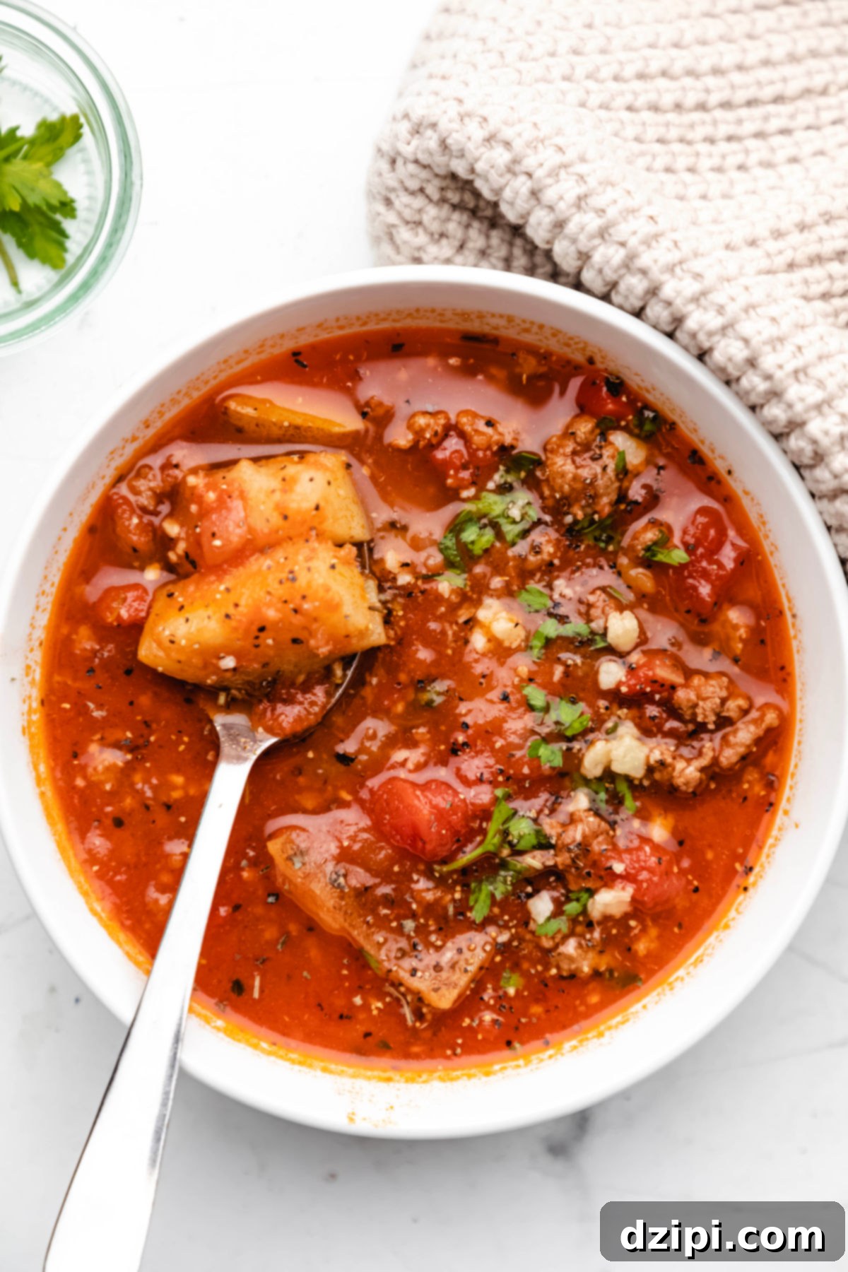 A vibrant bowl of bright red Instant Pot Hamburger soup, filled with chunky potatoes and seasoned ground beef, presented on a clean white background.