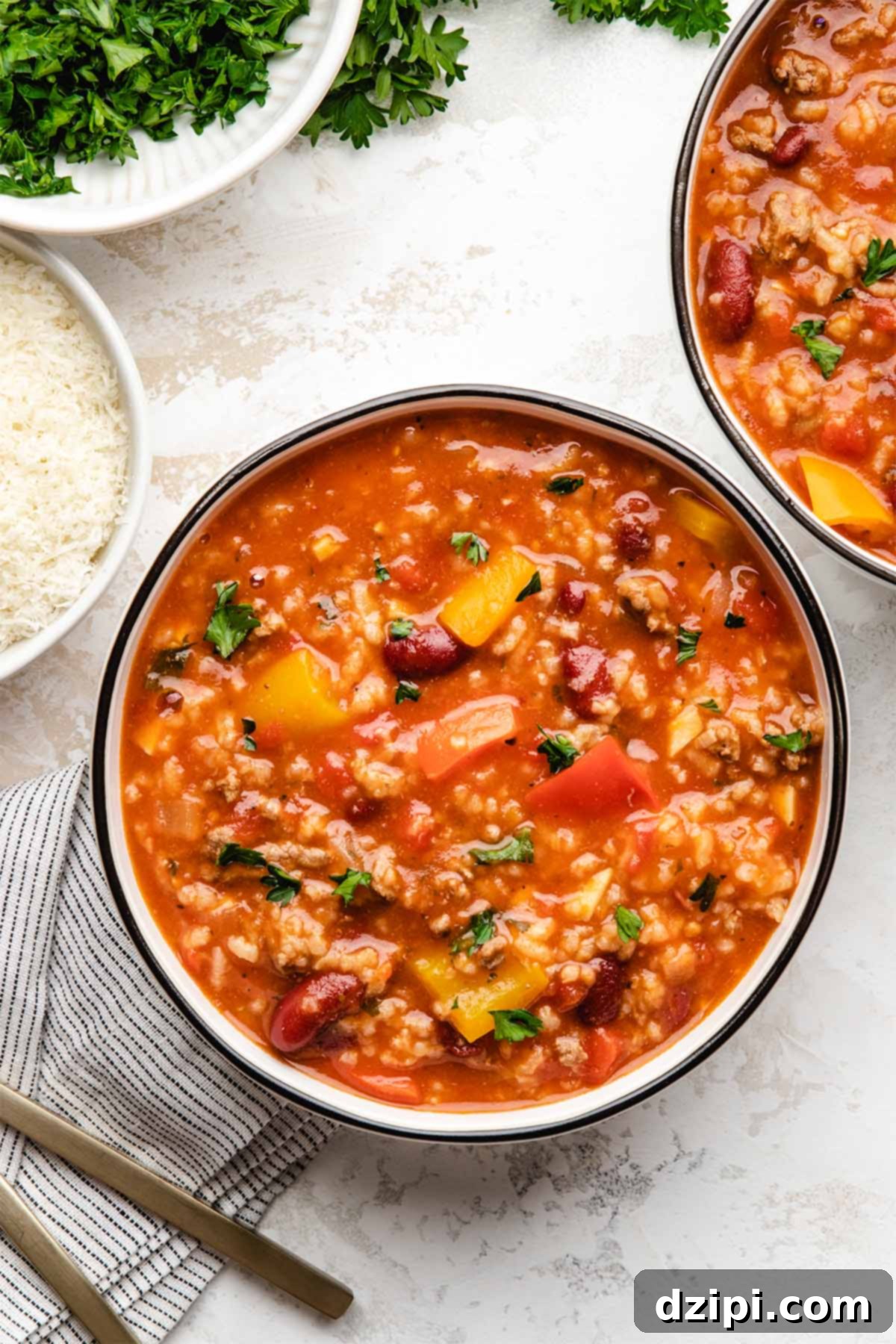 Two inviting bowls of Instant Pot stuffed pepper soup, brimming with colorful bell peppers, ground meat, rice, and beans, arranged on a light-colored background.