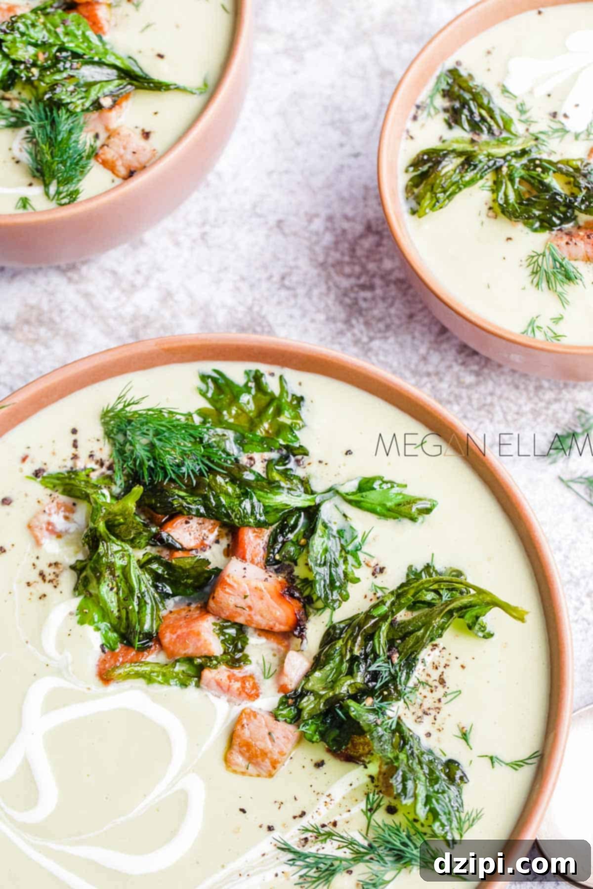 Three elegant bowls filled with light green celery soup, each artfully garnished with fresh celery leaves, delicate dill, and crispy "ham croutons," creating a sophisticated presentation.