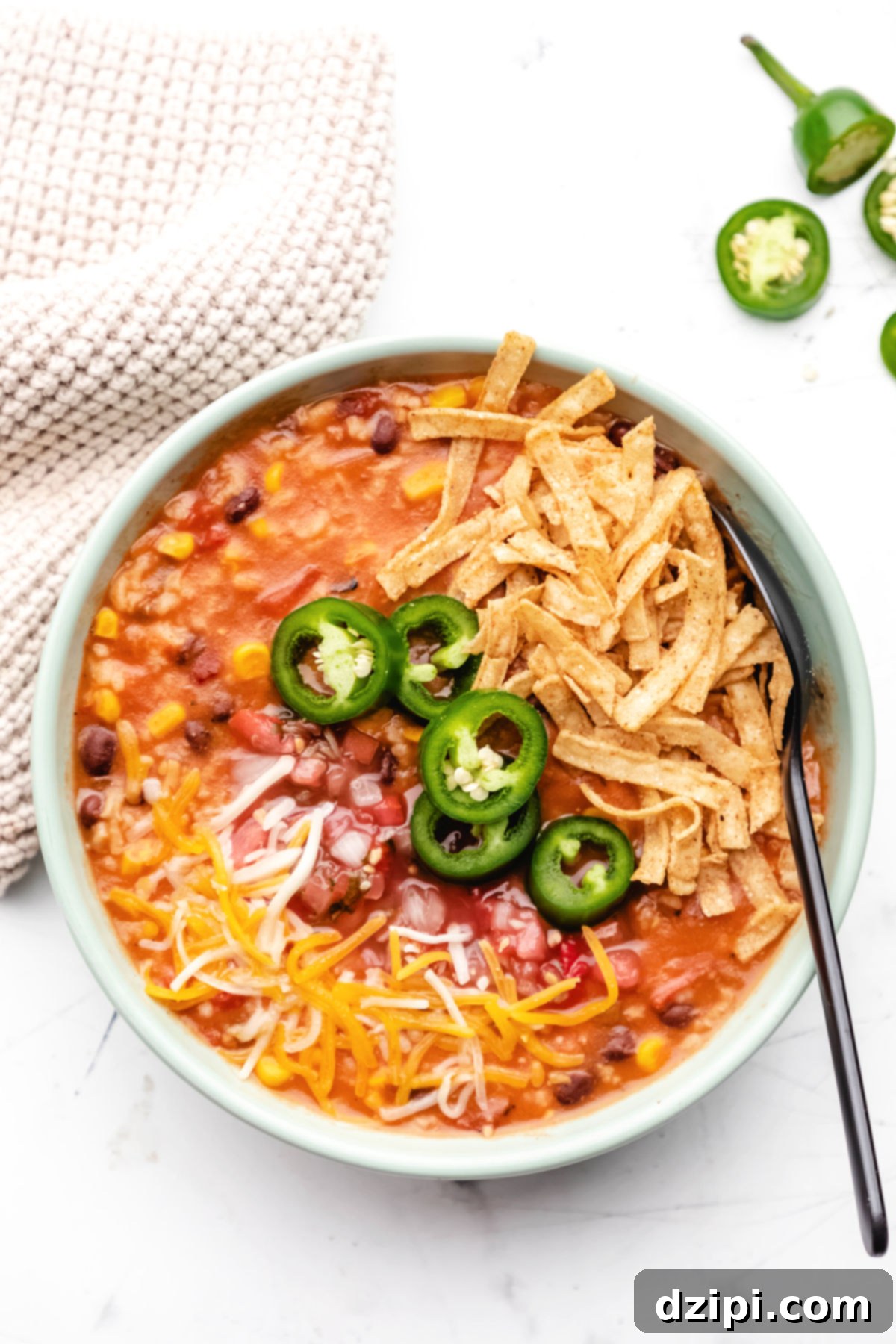 A inviting soup bowl filled with vibrant vegetarian tortilla soup, beautifully garnished with melted shredded cheese, thin slices of jalapeños, and crispy tortilla strips for texture.