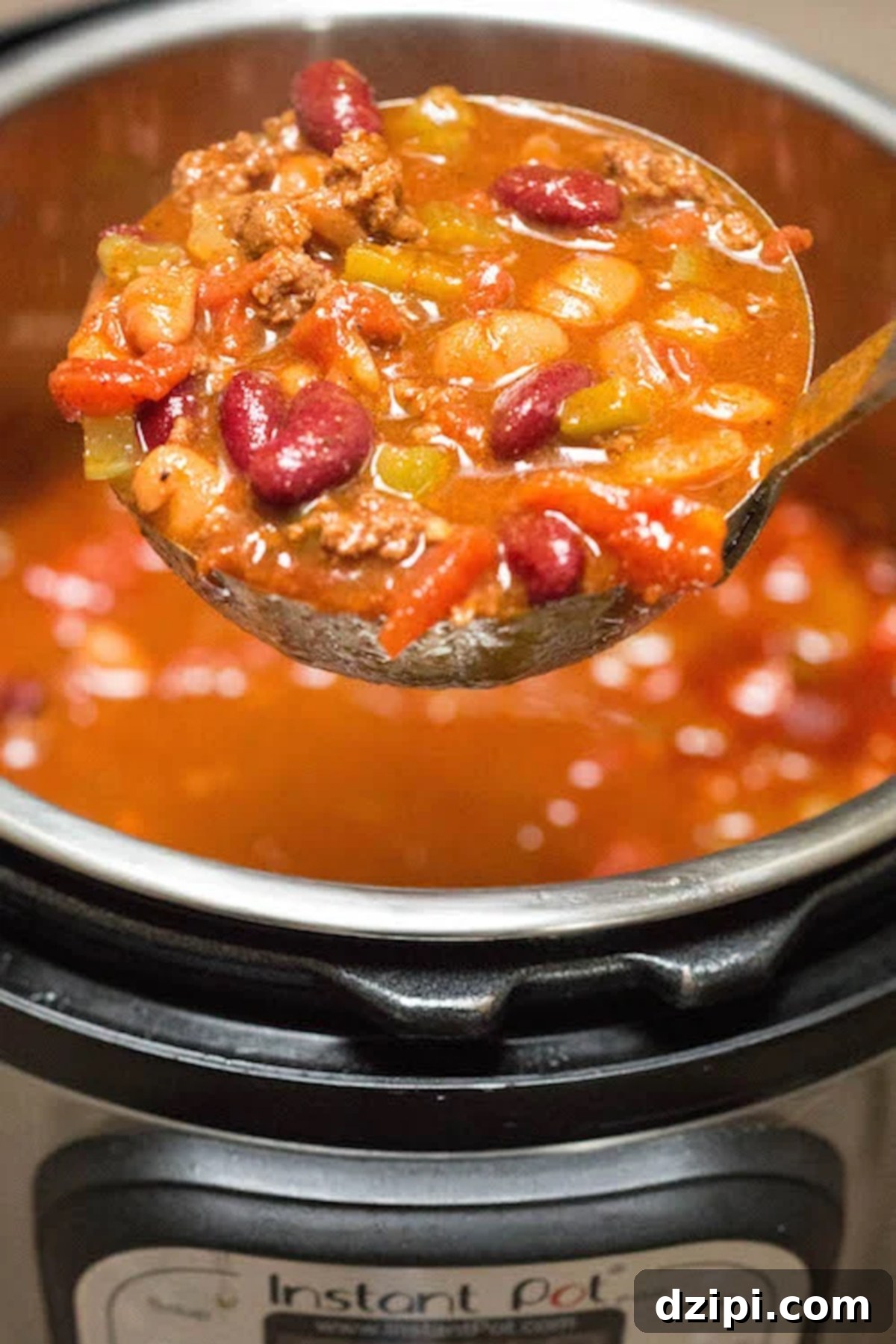 A ladle full of rich, copycat Wendy's Chili is perfectly in focus, poised above the Instant Pot, which is softly blurred in the background, emphasizing the freshly cooked meal.