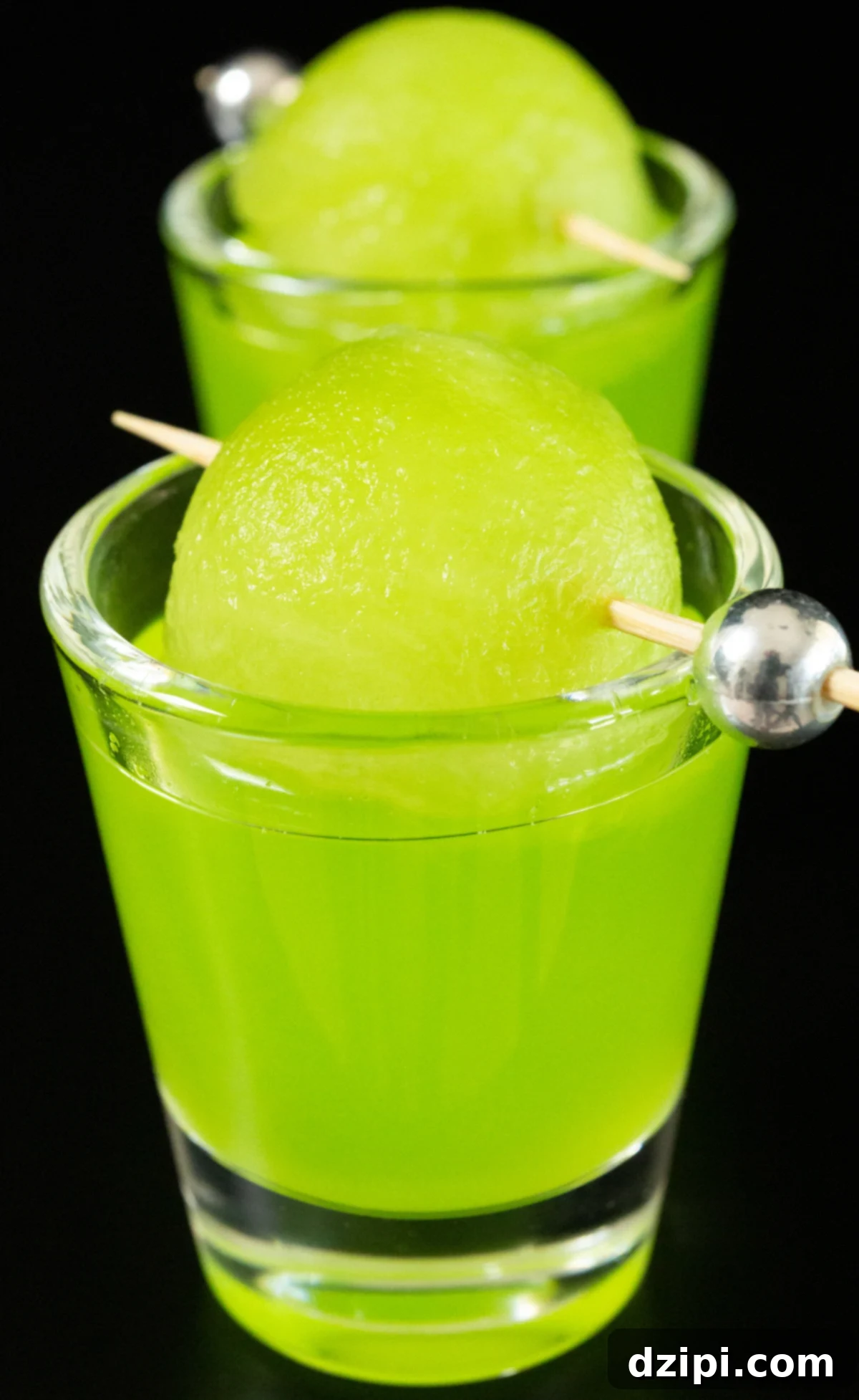 Two shot glasses filled with bright green melon ball shots on a black background.
