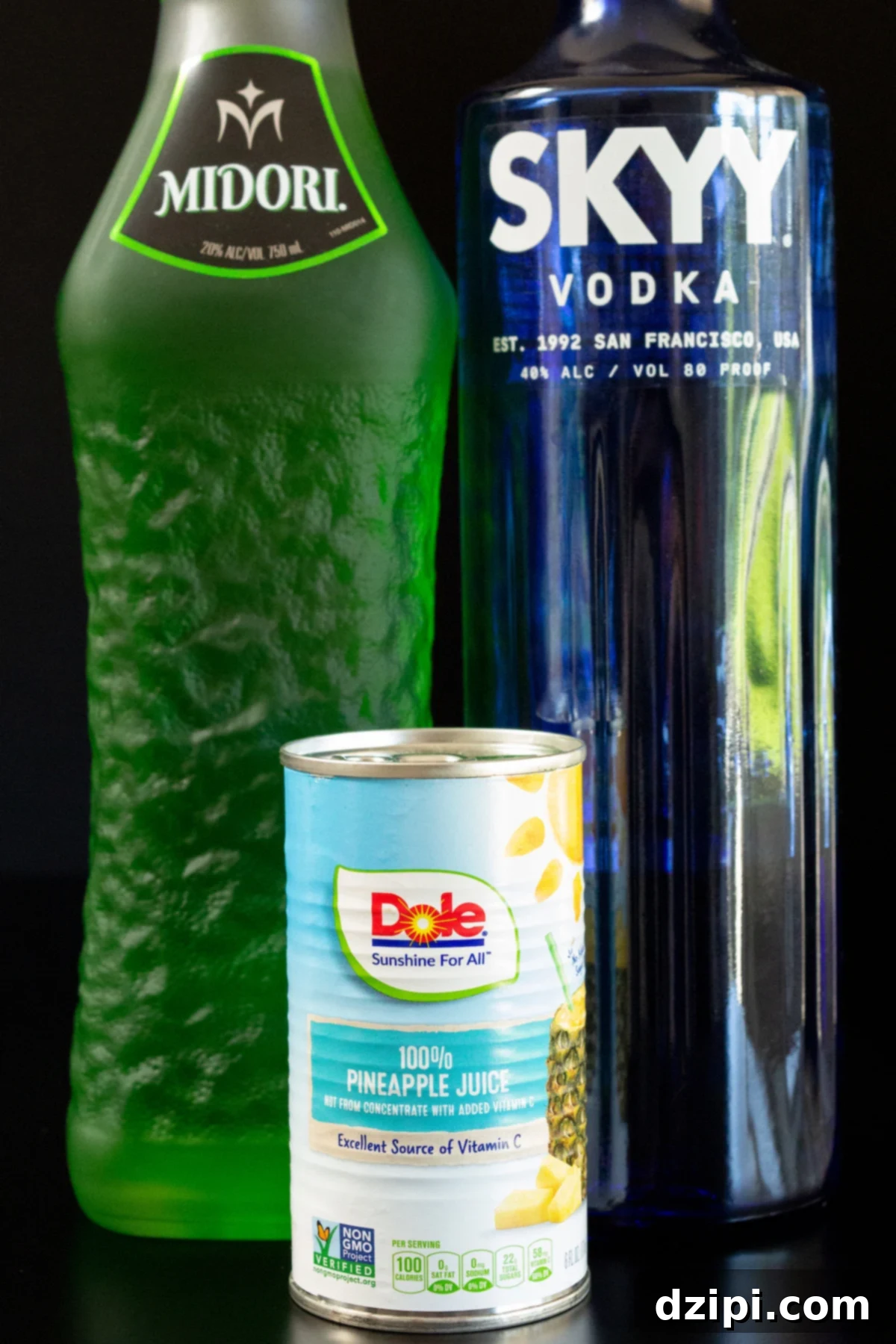 A bottle of Midori, Skyy Vodka, and a can of pineapple juice on a black background.