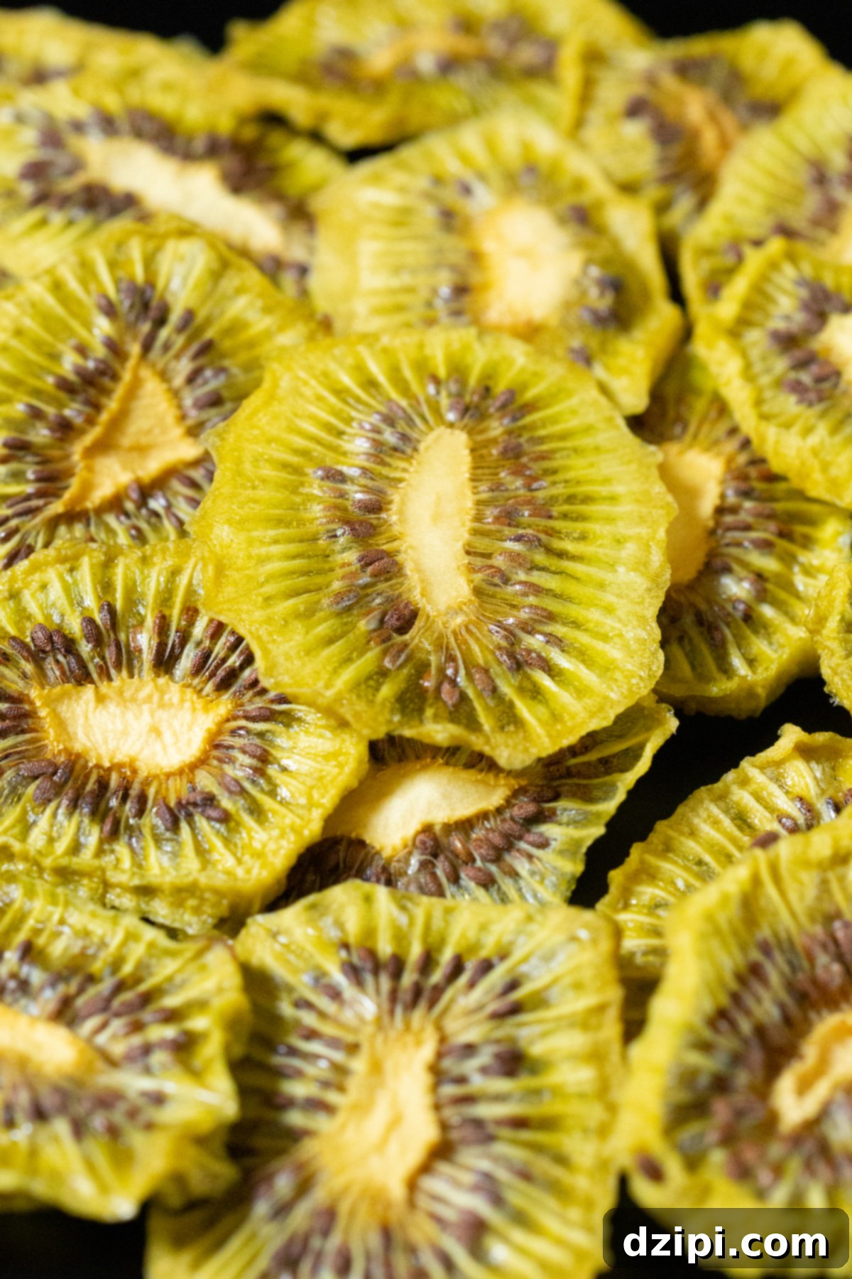 Dozens of dehydrated kiwi chips in a pile on a black background.