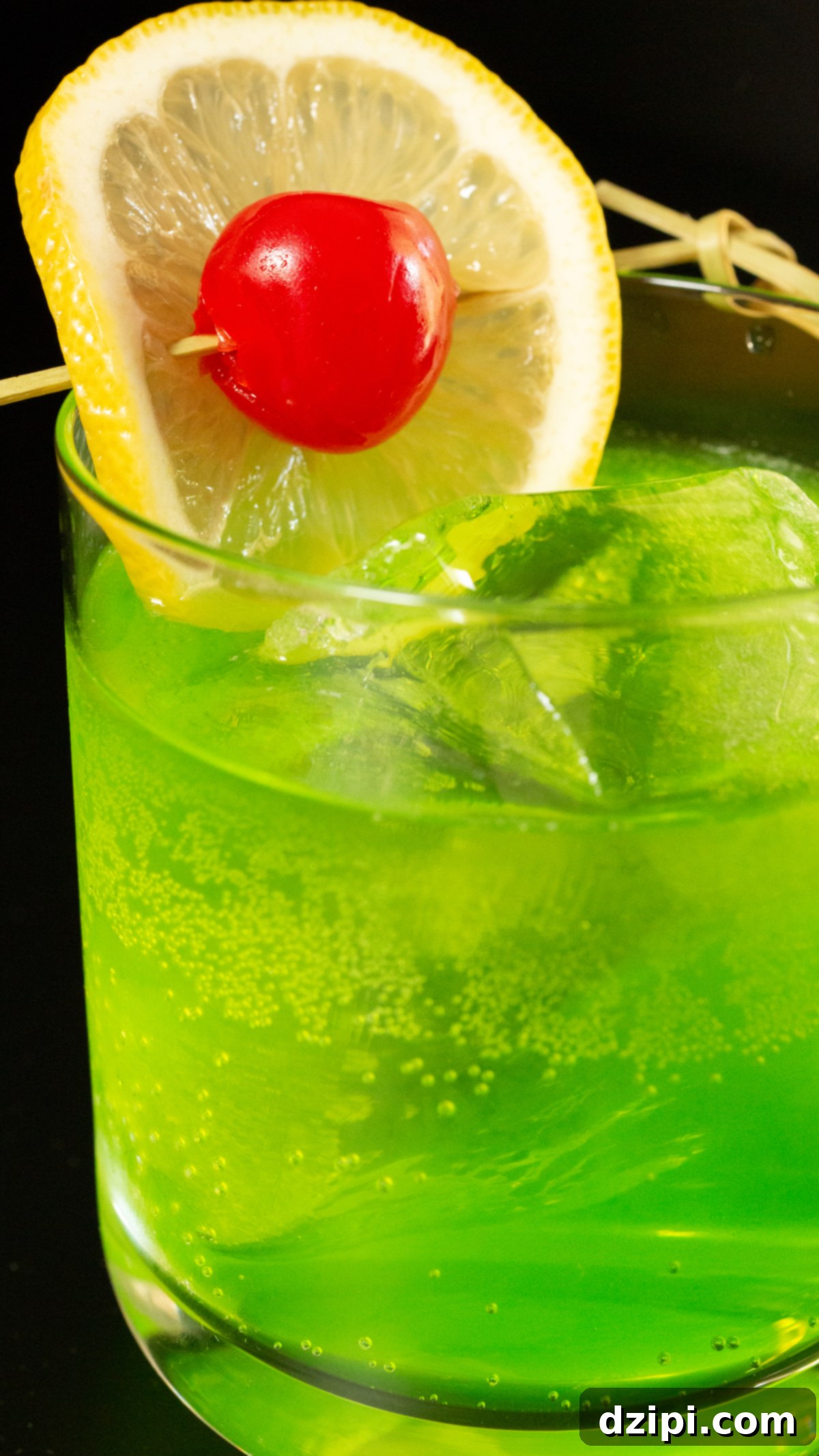 Radiant Melon Refresher 3 A lowball glass with a large block of ice is filled with a bright neon green Midori Sour cocktail that's garnished with a lime wheel and a maraschino cherry on a skewer.