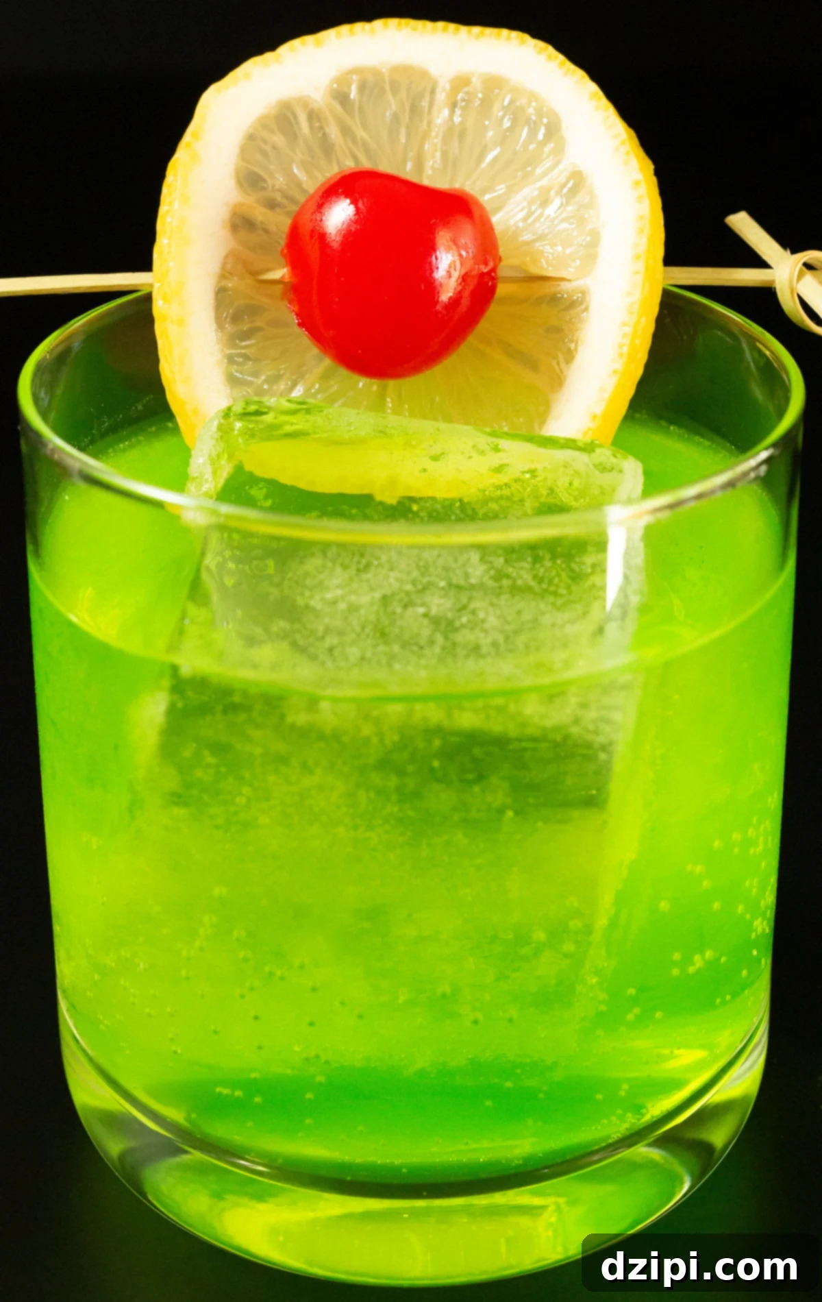 Radiant Melon Refresher 5 A lowball glass with a large block of ice is filled with a bright neon green Midori Sour cocktail that's garnished with a lime wheel and a maraschino cherry on a skewer.