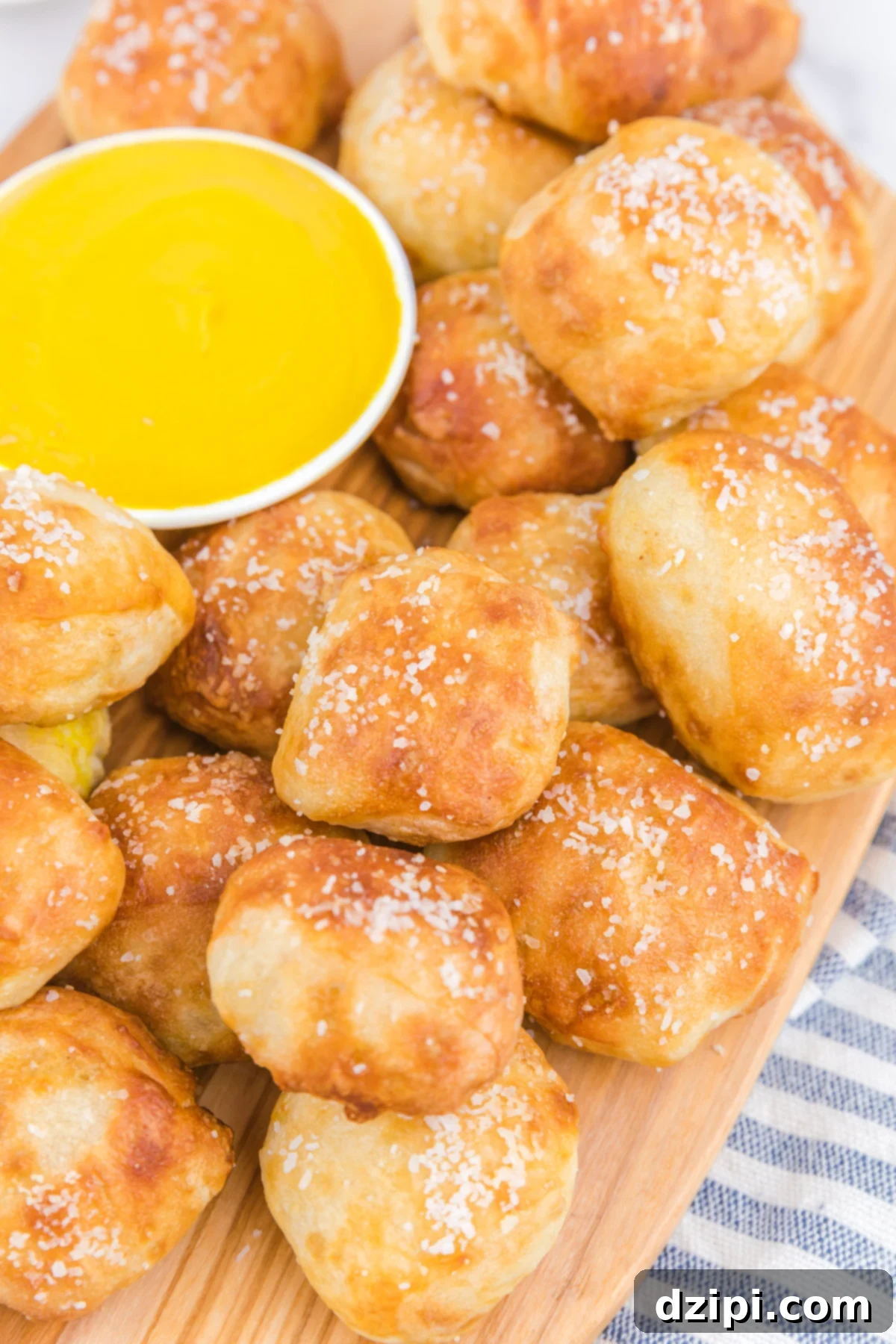 A cutting board showcasing dozens of golden air fryer pretzel bites, perfectly stacked next to a small bowl of classic yellow mustard, ready for dipping.