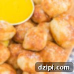 A cutting board with a few dozen air fryer pretzel bites stacked on it next to a small bowl of mustard.