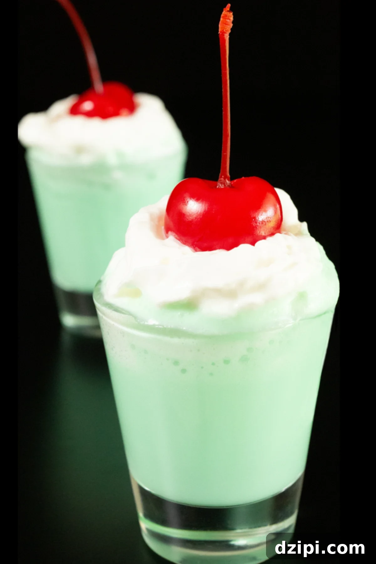 Emerald Elixir 8 Two shot glasses filled with mint green colored Shamrock Shots are topped with whipped cream and maraschino cherries, ready for a St. Patrick's Day toast.