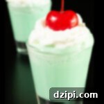 Emerald Elixir 4 Two shot glasses filled with mint green colored Shamrock Shots are topped with whipped cream and maraschino cherries.