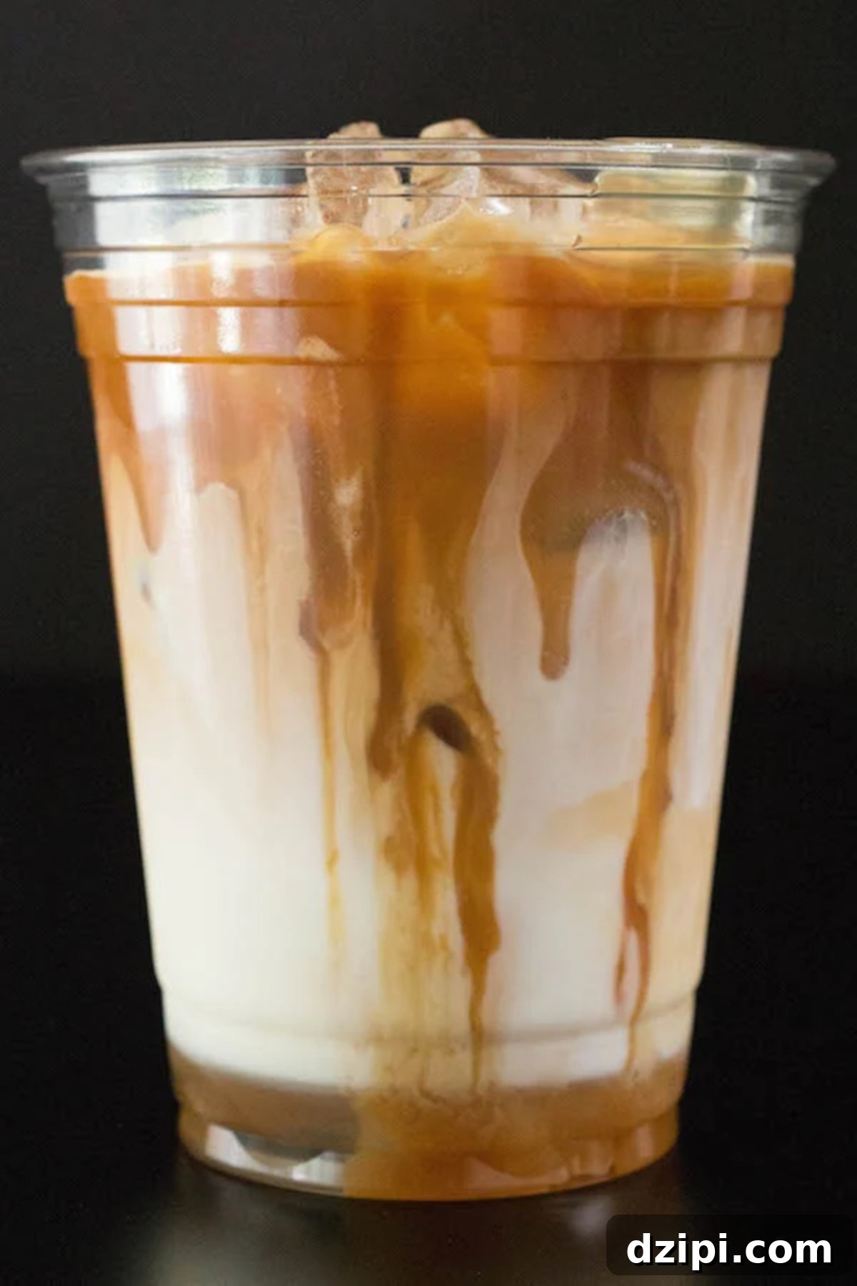 A clear plastic cup brimming with a beautifully layered caramel macchiato, with luscious caramel sauce artfully dripping down its sides.