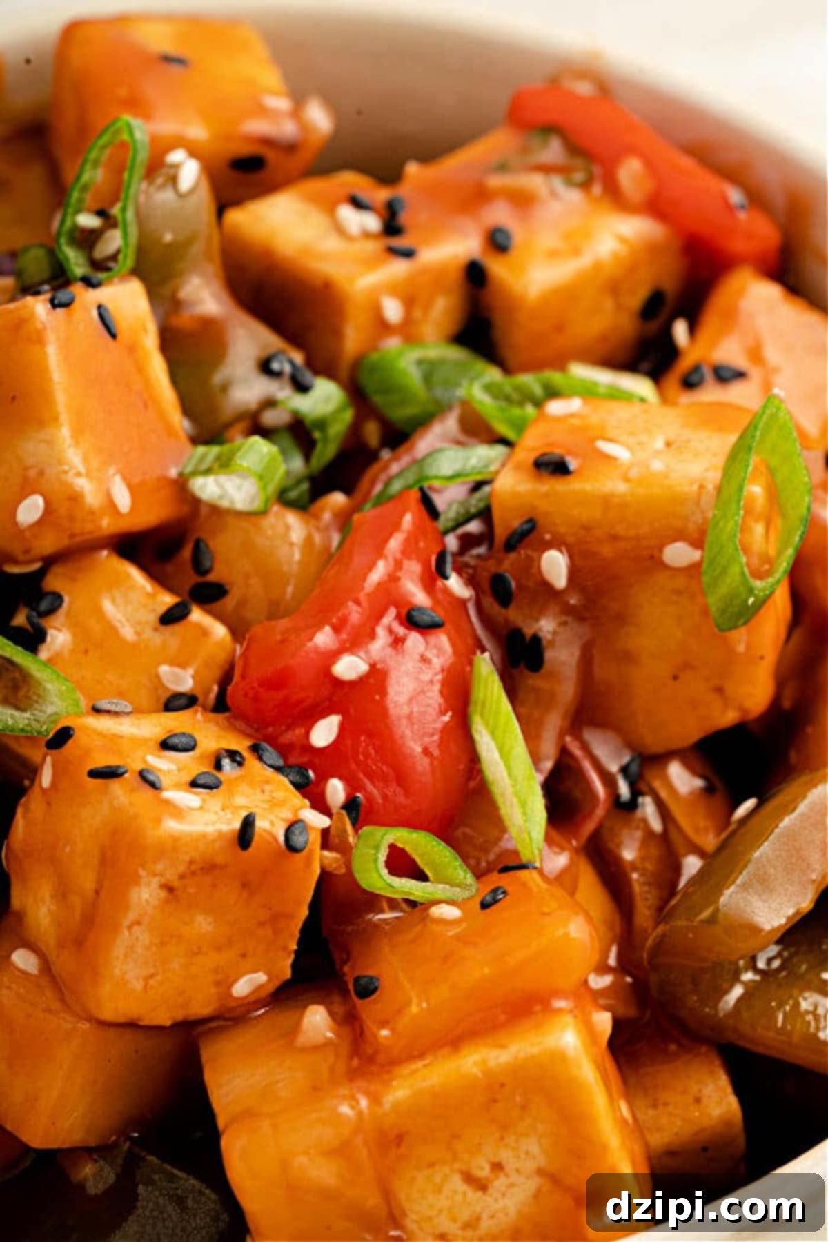 A vibrant dish of chopped chicken and vegetables, generously coated in shimmering copycat sweet & sour sauce and garnished with fresh sliced green onion and sesame seeds.