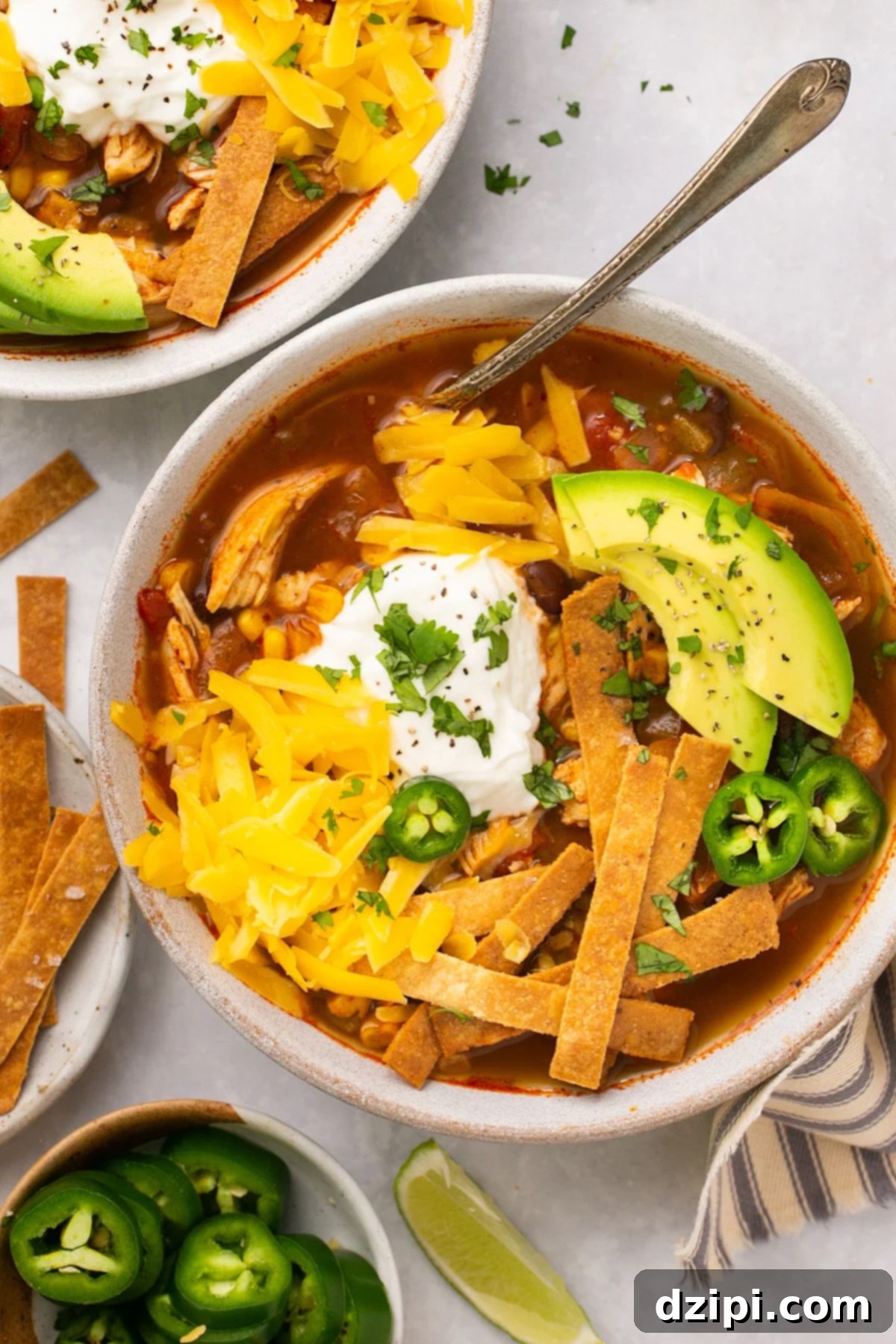 A comforting bowl of copycat Chick-fil-A tortilla soup, beautifully presented in a ceramic bowl and garnished with shredded cheddar cheese, sliced jalapeño and avocado, a dollop of sour cream, and crispy tortilla strips.