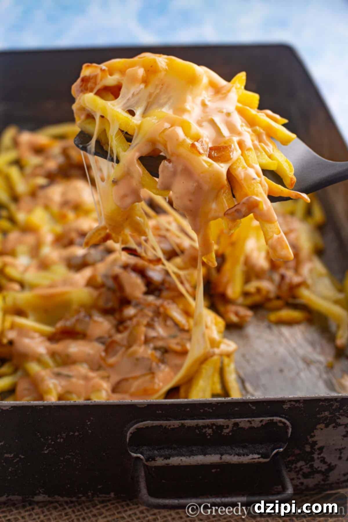 A spatula lifting a generous portion of homemade Animal Fries, loaded with melted American cheese and perfectly grilled onions.