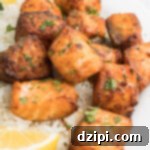 Bite sized pieces of salmon cooked in the air fryer on a white dinner plate with rice and lemon slices.