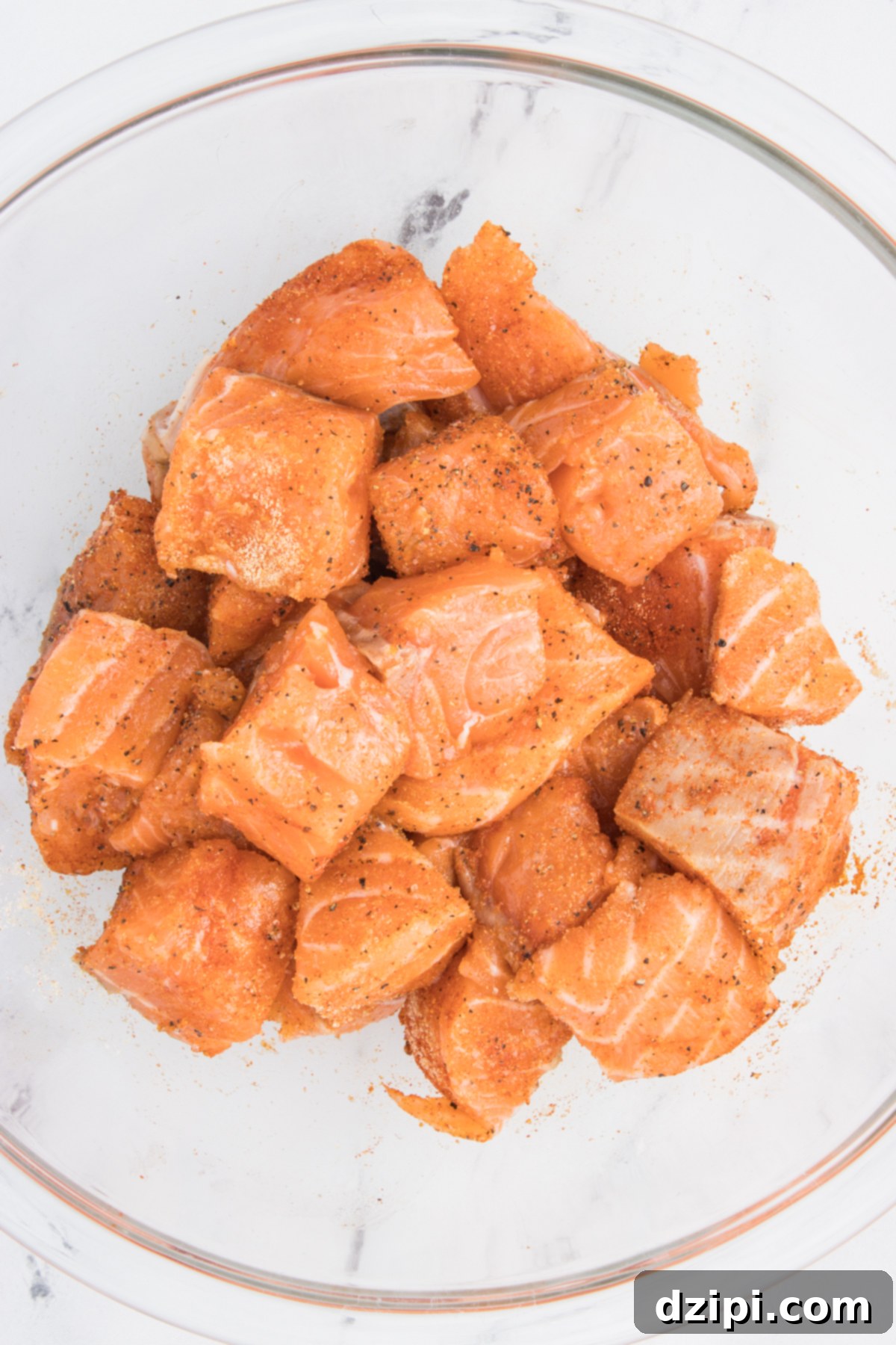 Fresh salmon that has been cut into cubes in a mixing bowl covered in seasoning.