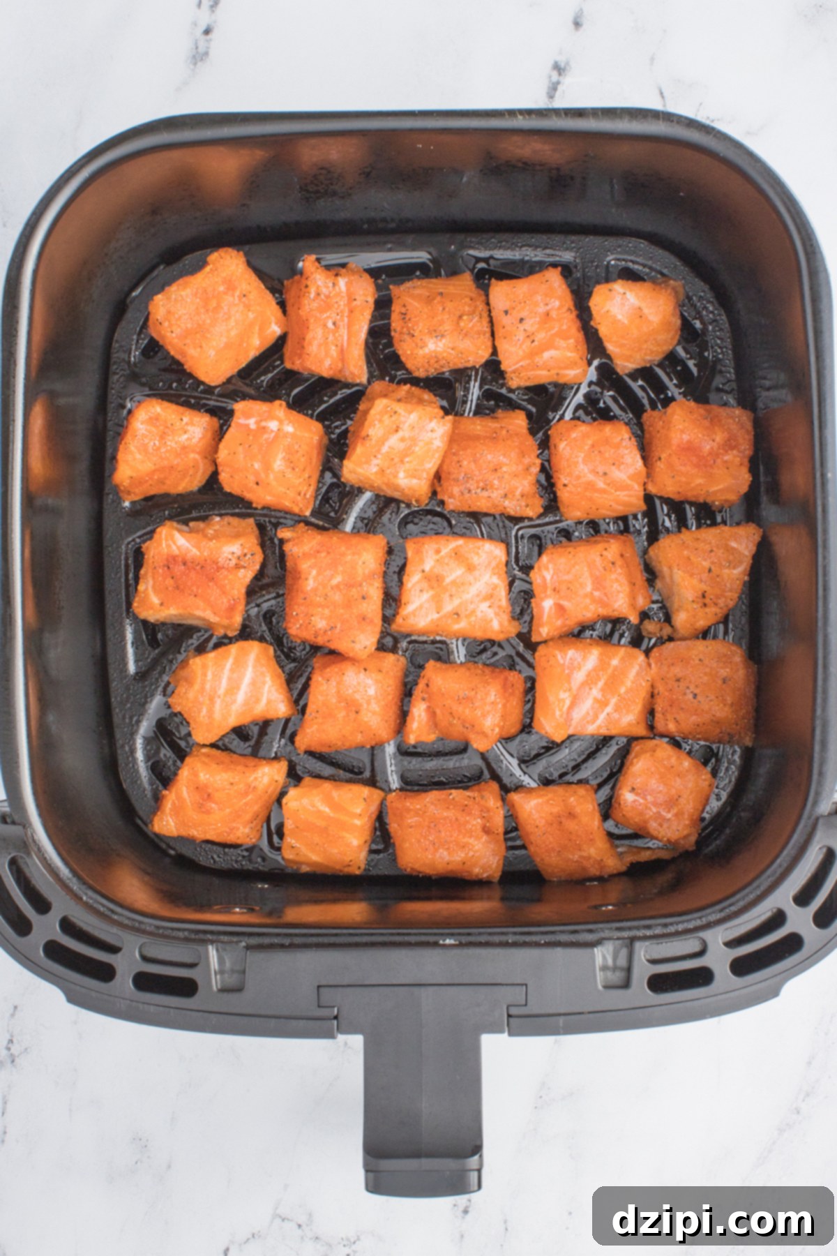 Raw seasoned cubed salmon bites in a single layer in an air fryer basket.