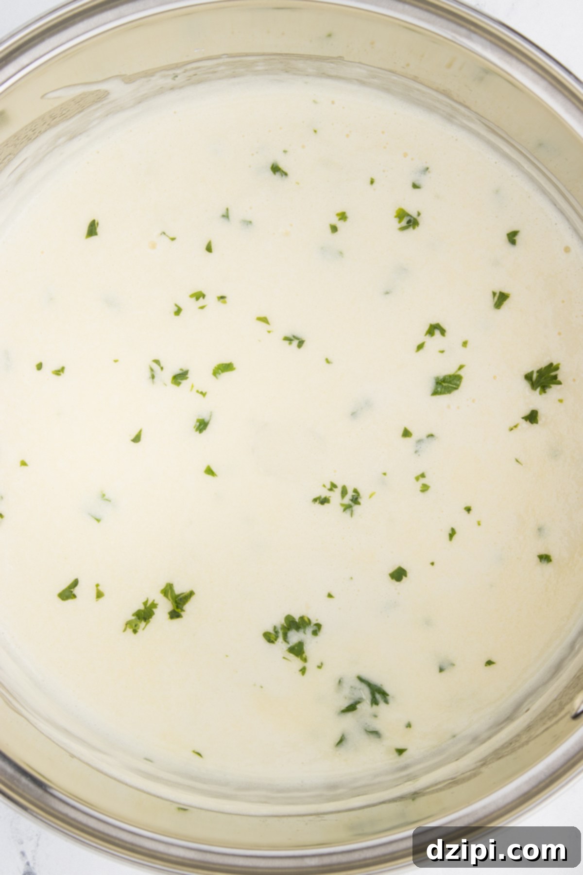 A small metal bowl with white garlic cream sauce that's garnished with fresh chopped parsley.