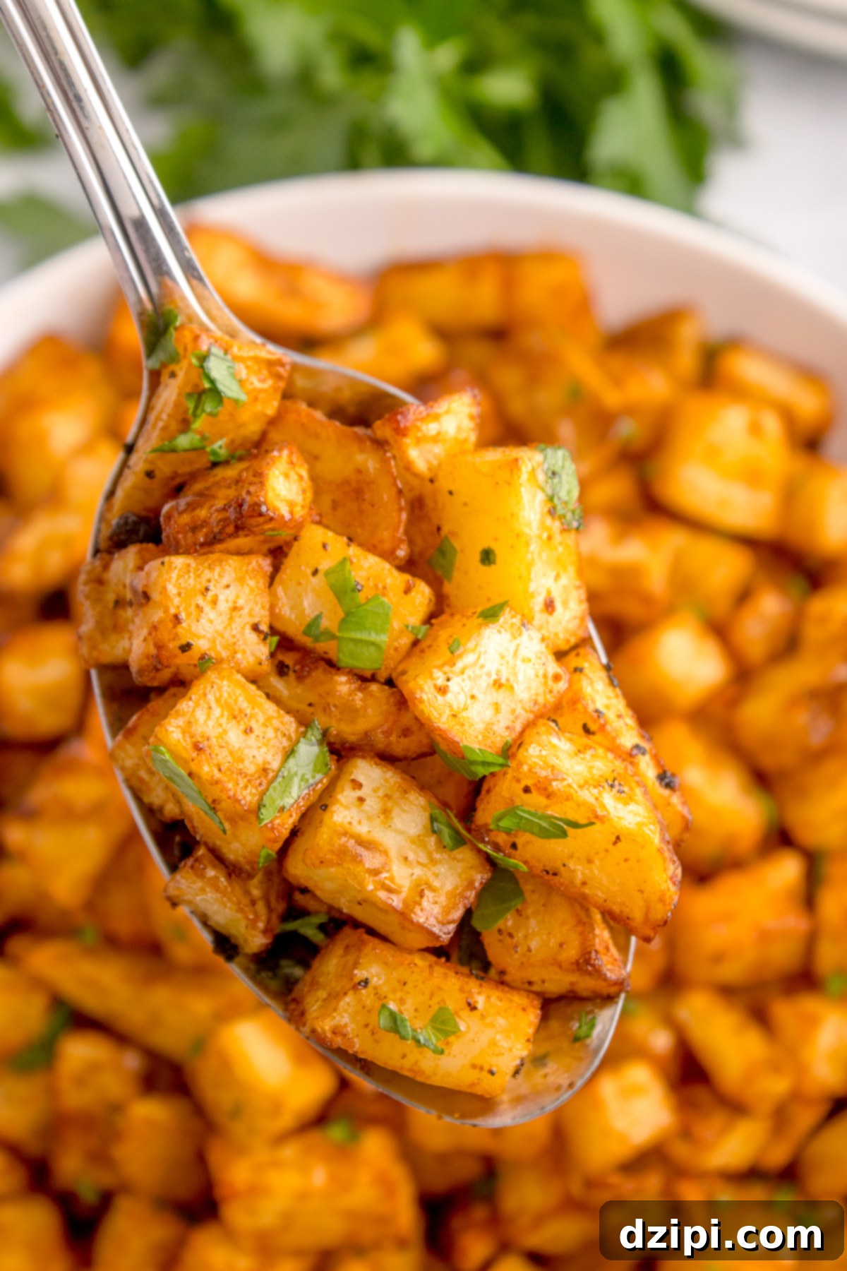 A serving spoon holding up diced air fried breakfast potatoes garnished with chopped parsley.