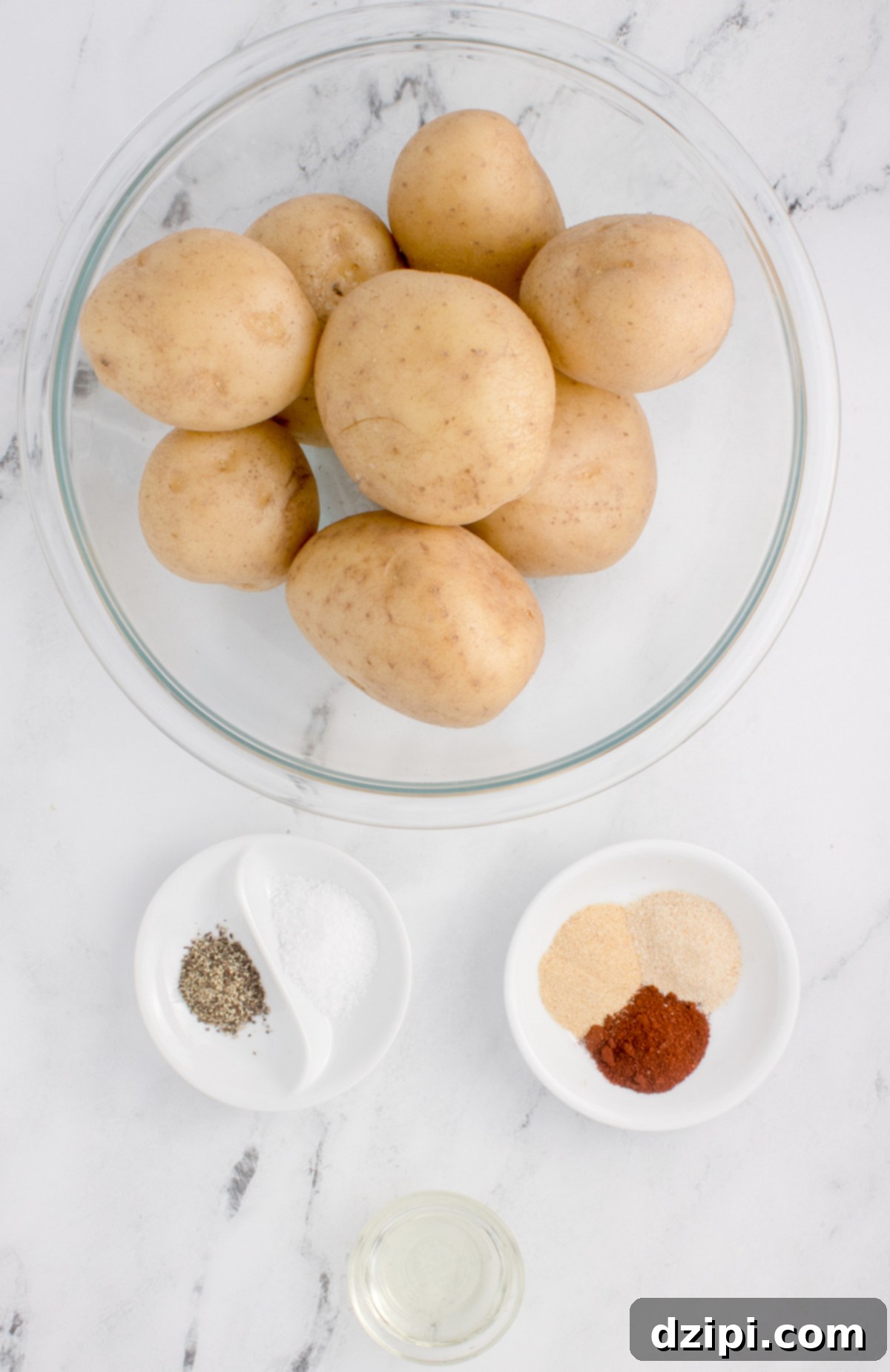 A bowl of potatoes next to two small bowls of seasonings and another small bowl of oil.