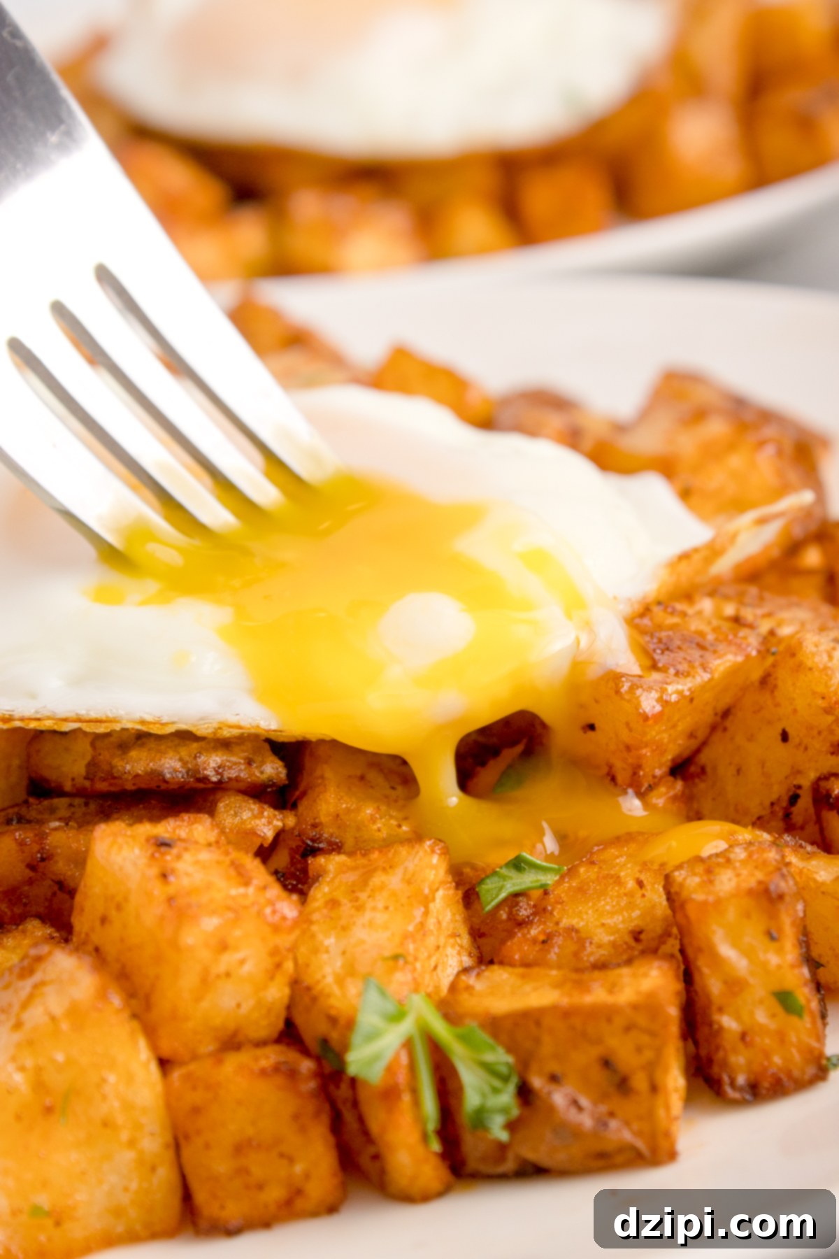 Diced air fried breakfast potatoes topped with a sunny-side up egg that's yolk is oozing out.