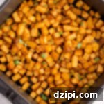 An air fryer basket filled with cooked diced breakfast potatoes that are garnished with chopped parsley.