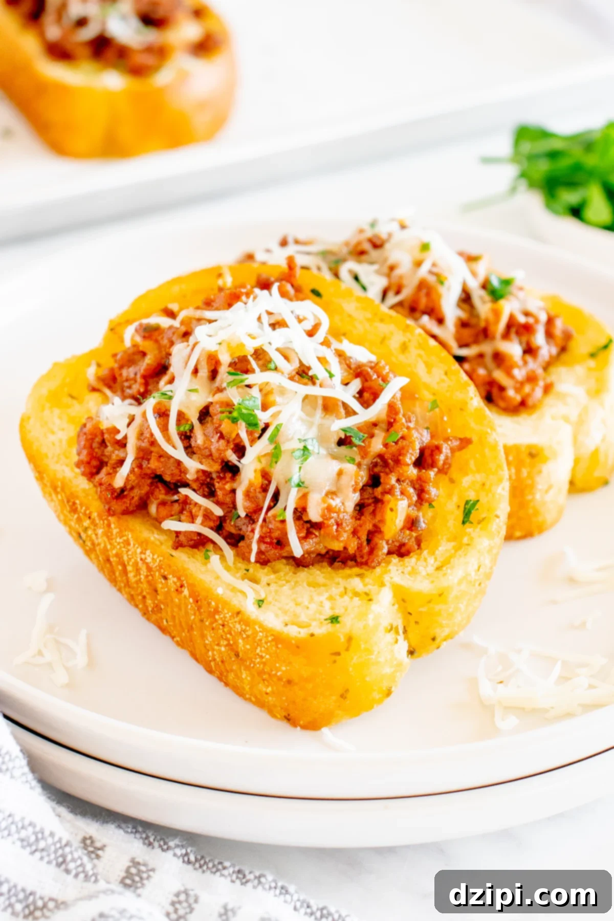 Sloppy Joe Texas Toast Melts 3 A white serving plate featuring two slices of Texas Toast, generously topped with sloppy Joe mixture and a blanket of melted shredded mozzarella cheese, garnished with fresh parsley.