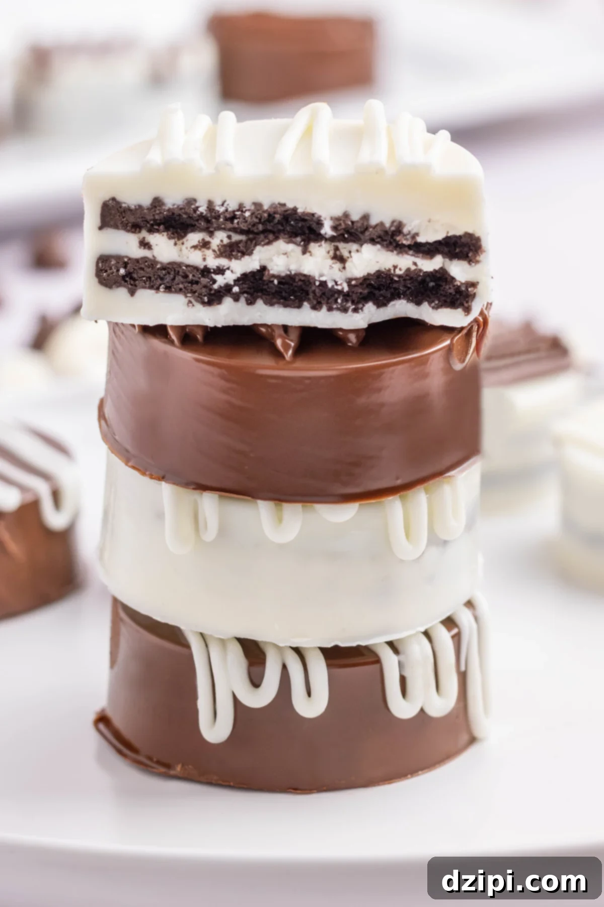 Four white and milk chocolate covered Oreos stacked on top of each other. The top one is cut in half to see the cookie inside.