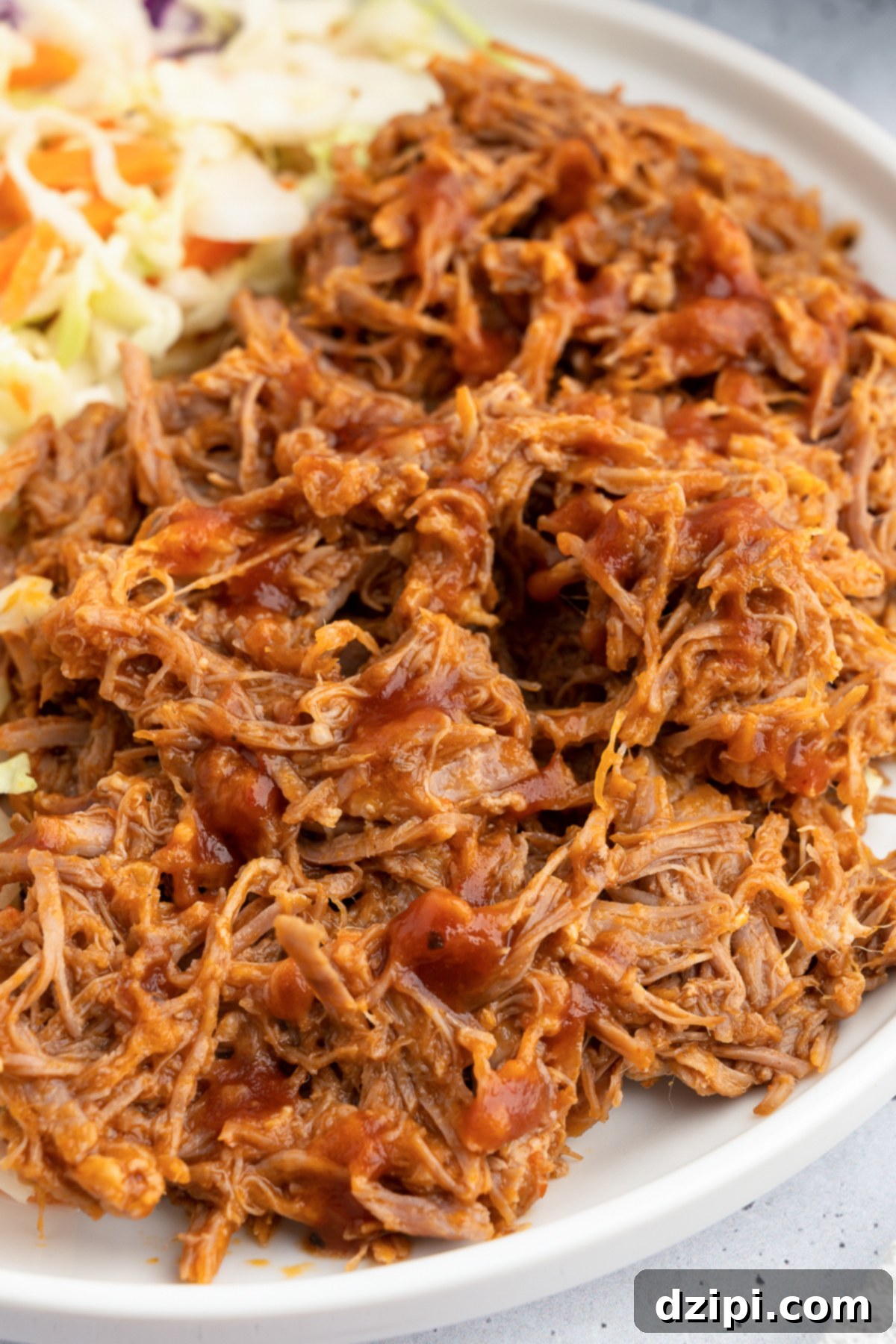 Juicy Instant Pot Pulled Pork 6 Half of a dinner plate showcasing a generous serving of perfectly shredded pulled pork, with the other half blurred, featuring a vibrant side of coleslaw.