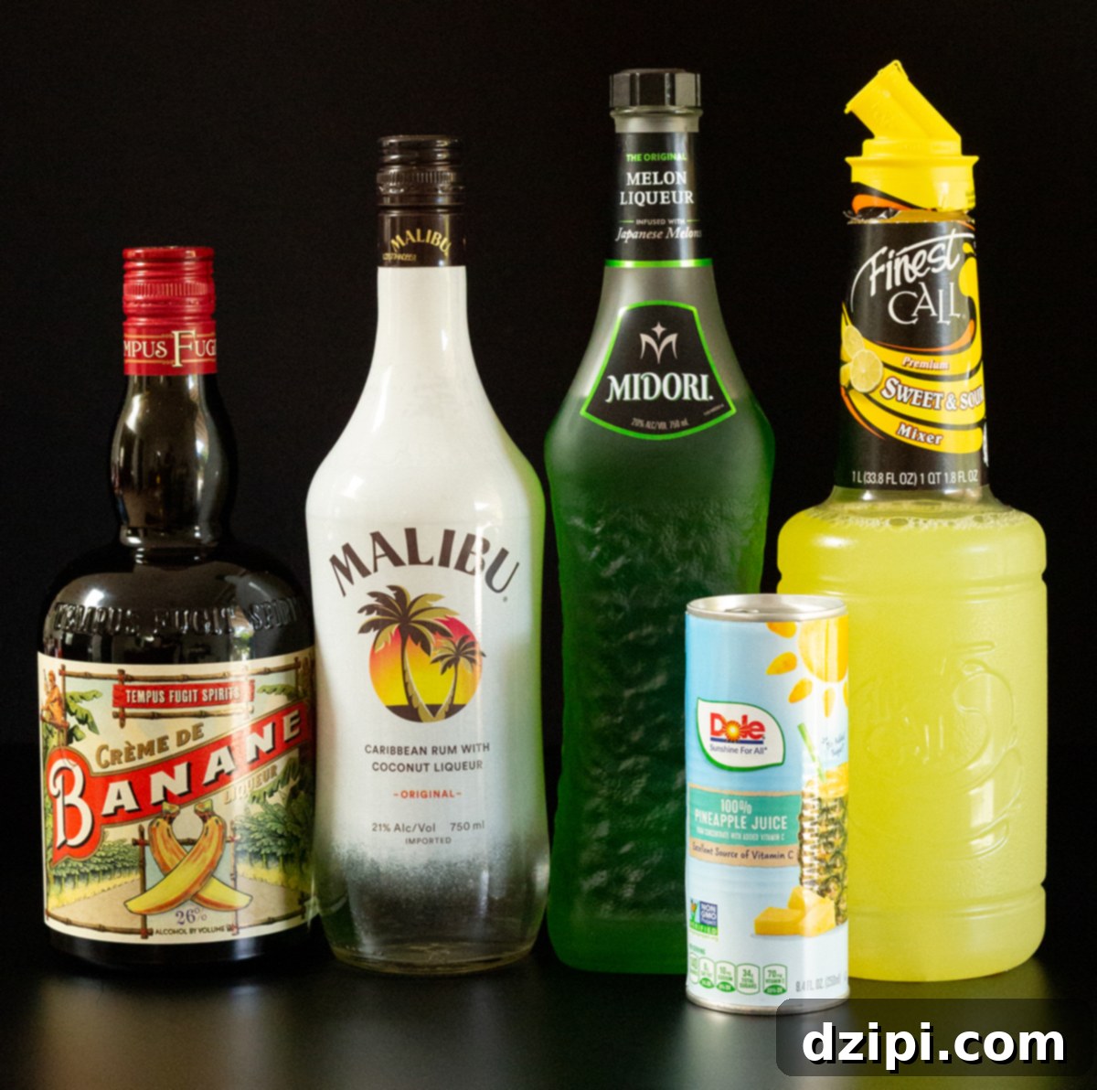 A vibrant display of key June Bug cocktail ingredients on a sleek black background: a bottle of banana liqueur, Malibu coconut rum, the distinctive green Midori melon liqueur, a jug of sweet & sour mix, and a can of pineapple juice.