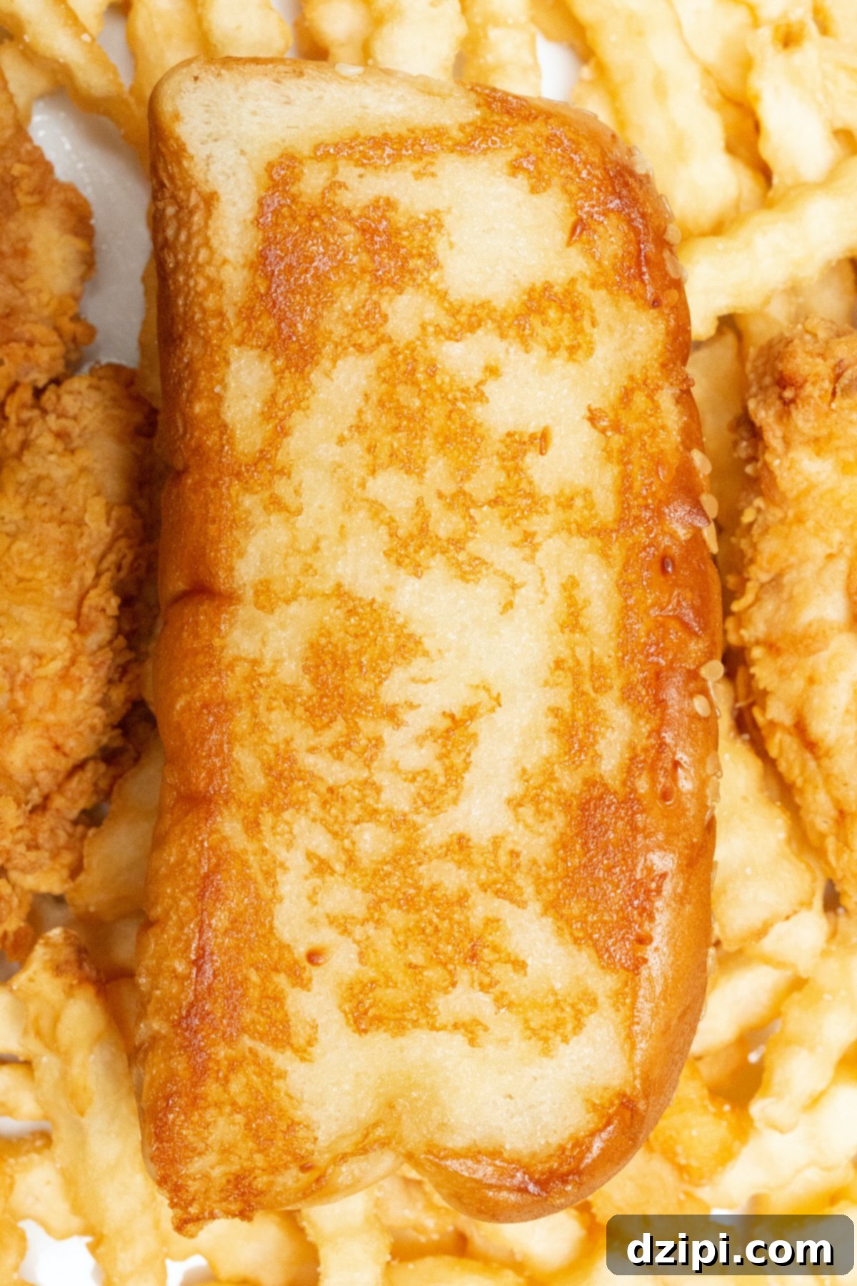 A slice of homemade Raising Canes bread on top of crinkly fries next to chicken tenders.