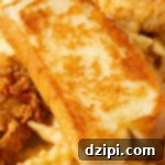 A slice of homemade Raising Canes garlic bread on top of crinkly fries and chicken tenders.