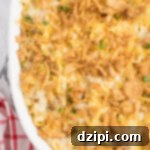 Close up of French onion chicken casserole topped with crispy onions in a white casserole dish.