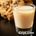 Oatmeal Cookie Cups 7 A shot glass filled with a creamy brown oatmeal cookie shot. Cookies are out of focus in the background.