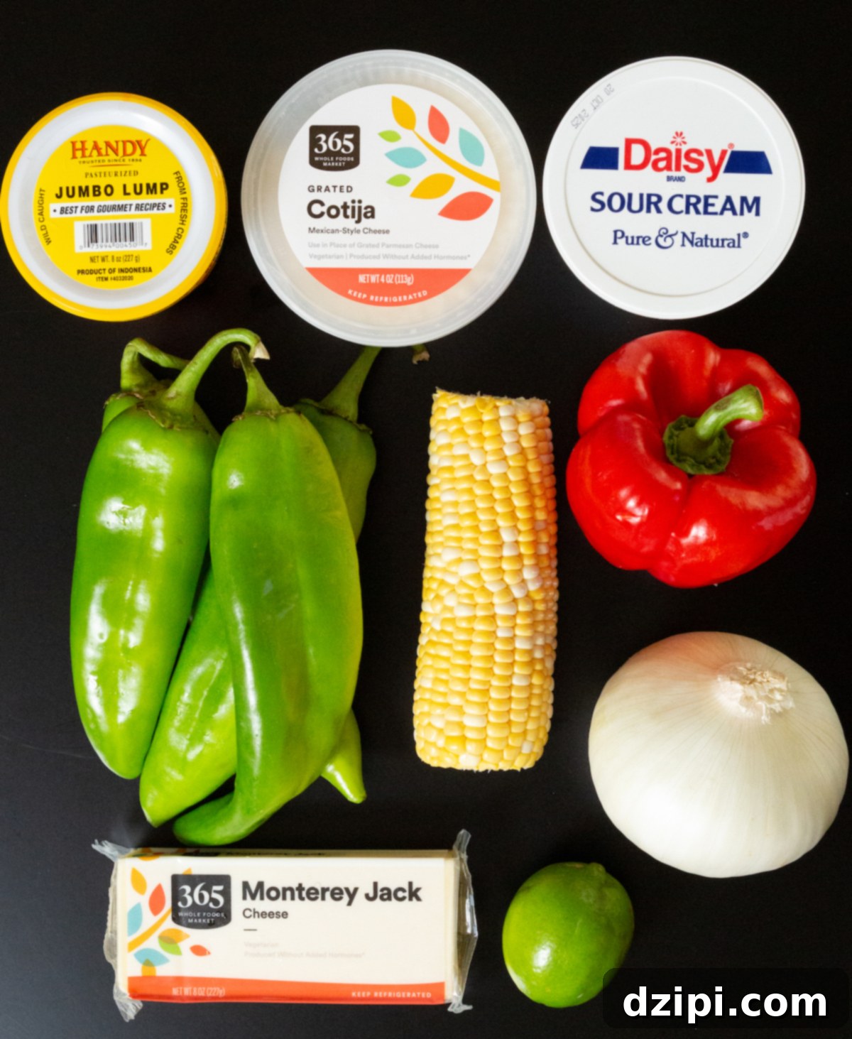 A container of lump crab, Donita cheese, sour cream, fresh hatch peppers, corn on the cob, red bell pepper, a white onion, a lime, and a block of Monterey Jack cheese.