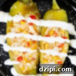 A small black plate with two large hatch peppers that have been stuffed with crab, corn, red bell pepper, and cheese. They ache been drizzled with lime crema and sprinkled with cojita cheese.