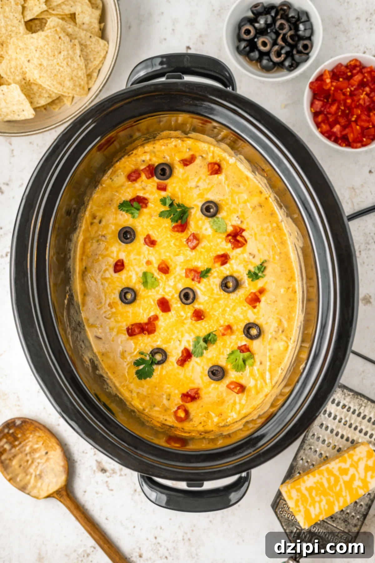 A Crock-Pot filled with a bubbling taco dip, richly topped with melted cheese, vibrant diced tomatoes, thinly sliced black olives, and fresh chopped cilantro. The dip looks hearty and inviting, perfect for scooping.