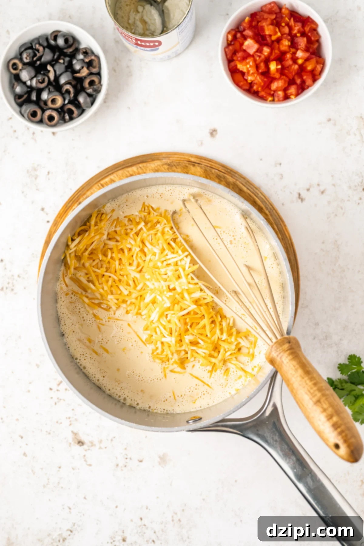 A small saucepan on the stove containing evaporated milk and shredded cheese, beginning to melt and combine into a creamy sauce.