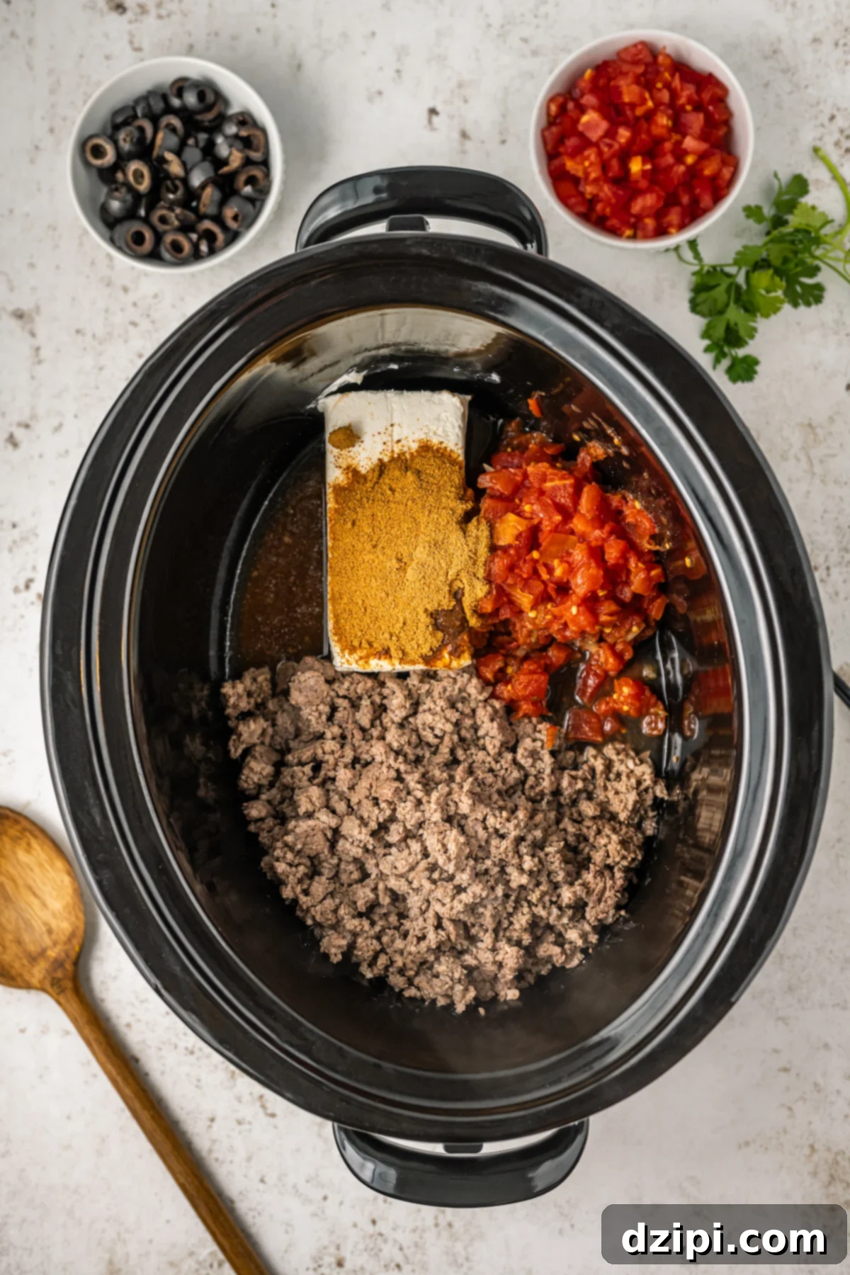 A Crock-Pot containing the browned ground beef, a can of Rotel, and taco seasoning, ready for the cheese sauce to be added.