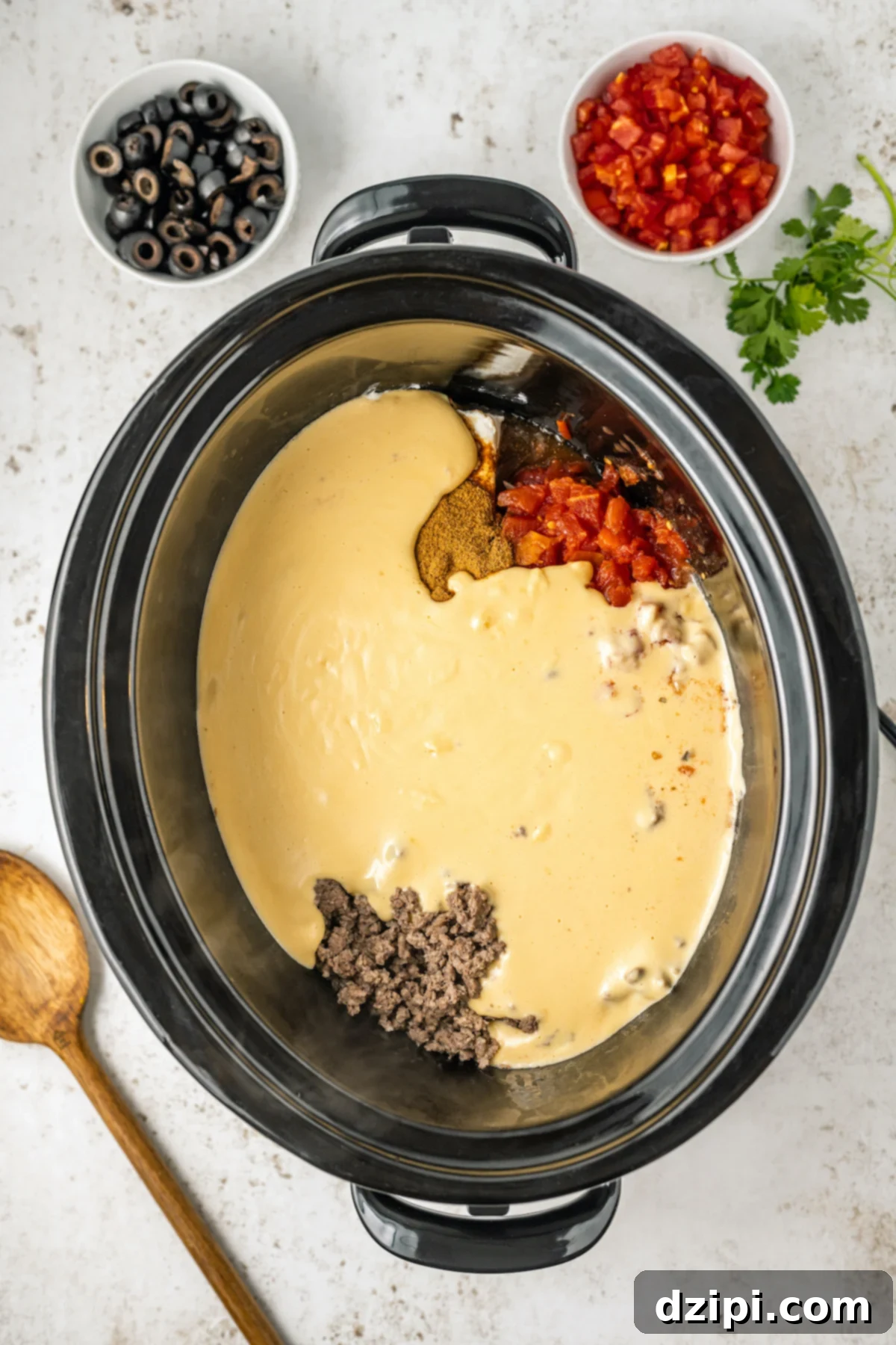 The Crock-Pot with browned ground beef, cream cheese, Rotel, and spices now covered with the creamy, homemade queso, ready for slow cooking.