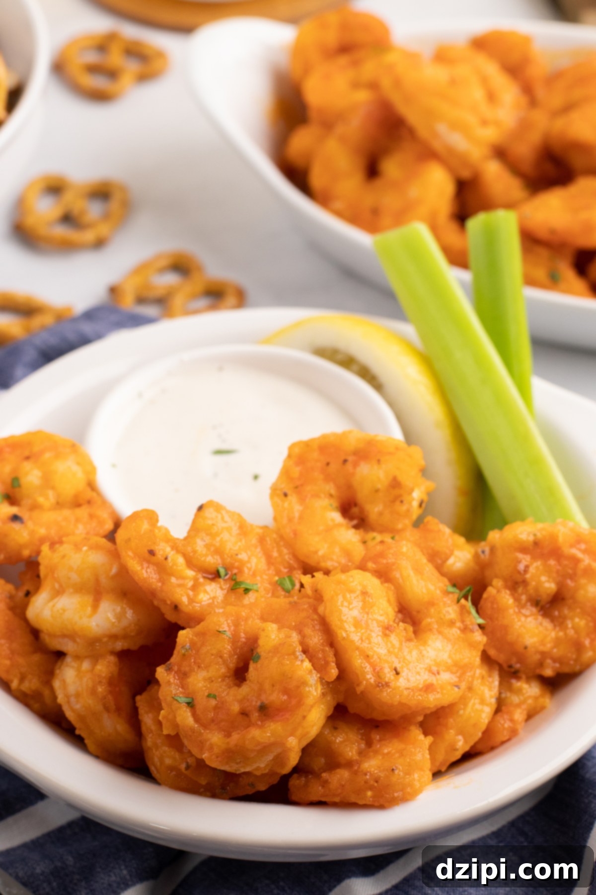 A white serving bowl with a dozen buffalo shrimp, a ramekin of ranch, and two celery sticks.