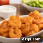 A white serving dish filled with buffalo shrimp. Hot sauce, ranch, and celery sticks out of focus in background.
