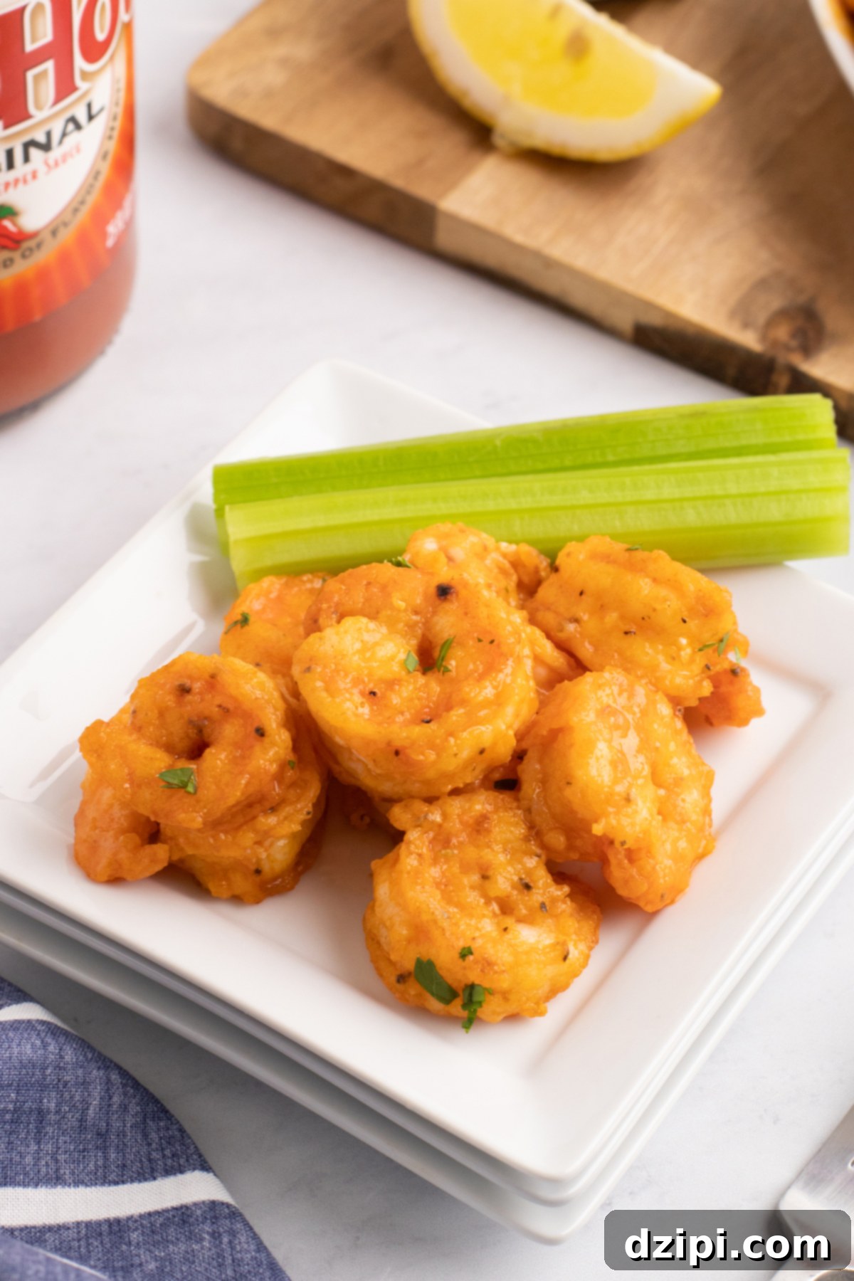 A small serving dish with six buffalo shrimp and a celery stick.