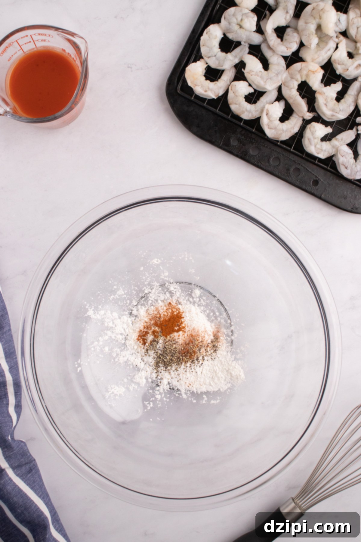 A mixing bowl filled with cornstarch and spices. A pan of raw shrimp is next to it.